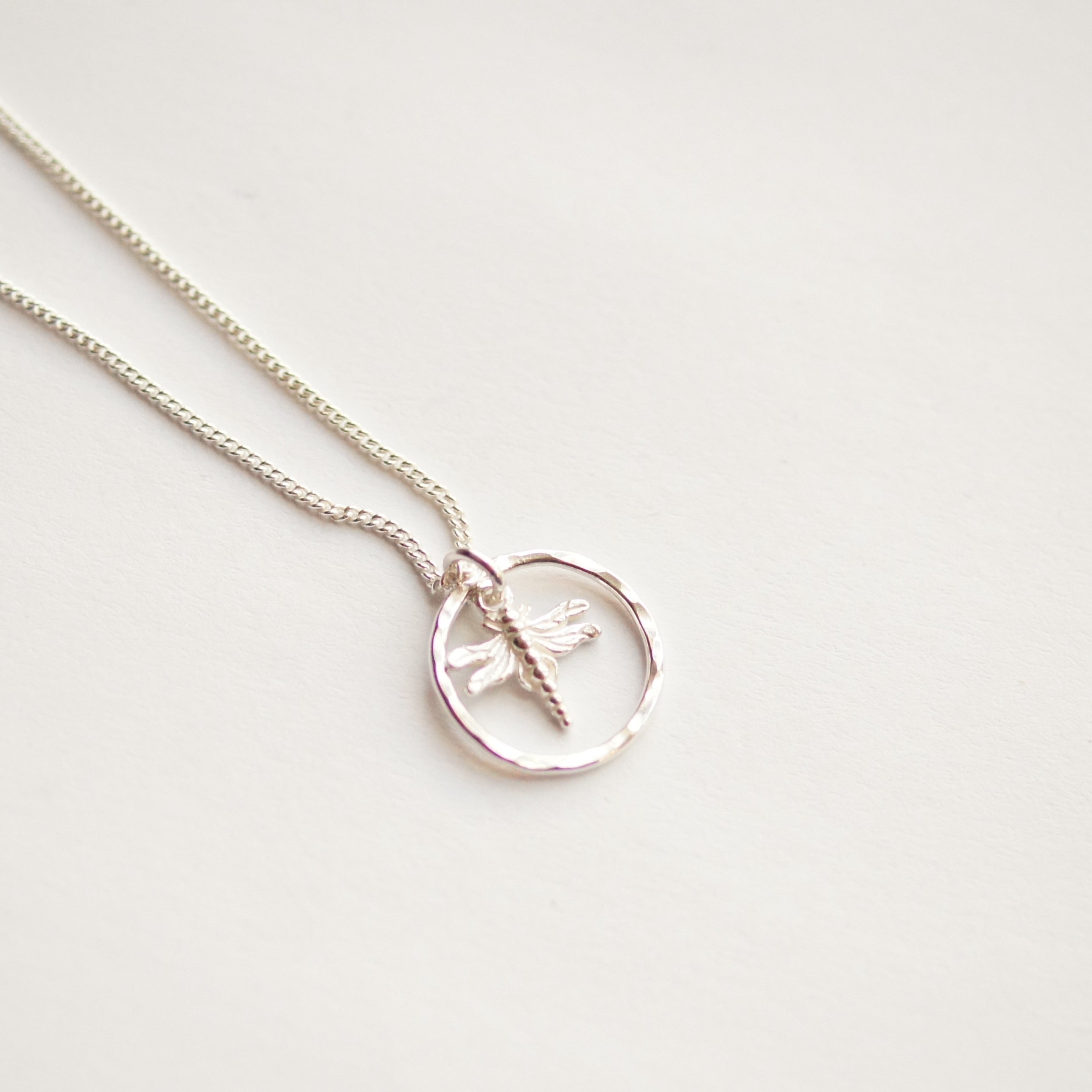 Silver necklace with a dragonfly pendant on a light gray background