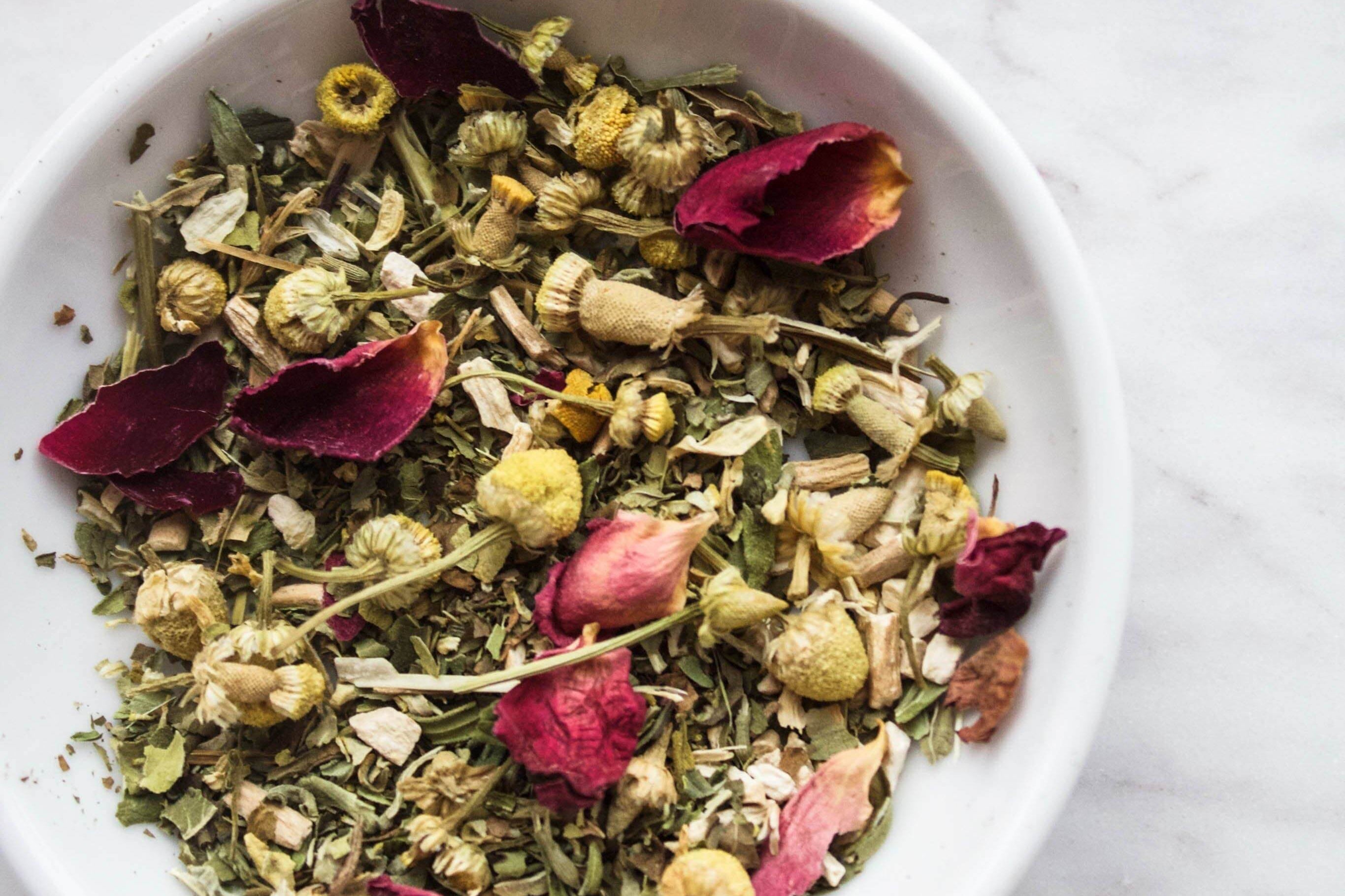 Organic herbal tea blend with chamomile, peppermint, and rose petals in a white bowl.