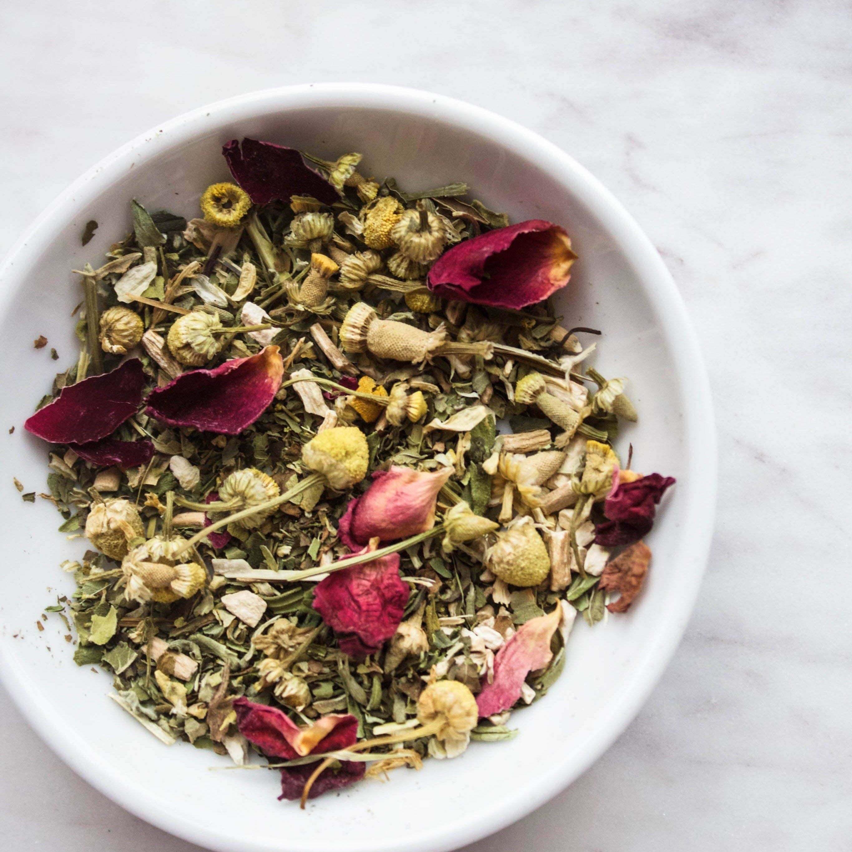 Organic herbal tea blend with chamomile, peppermint, and rose petals in a white bowl.