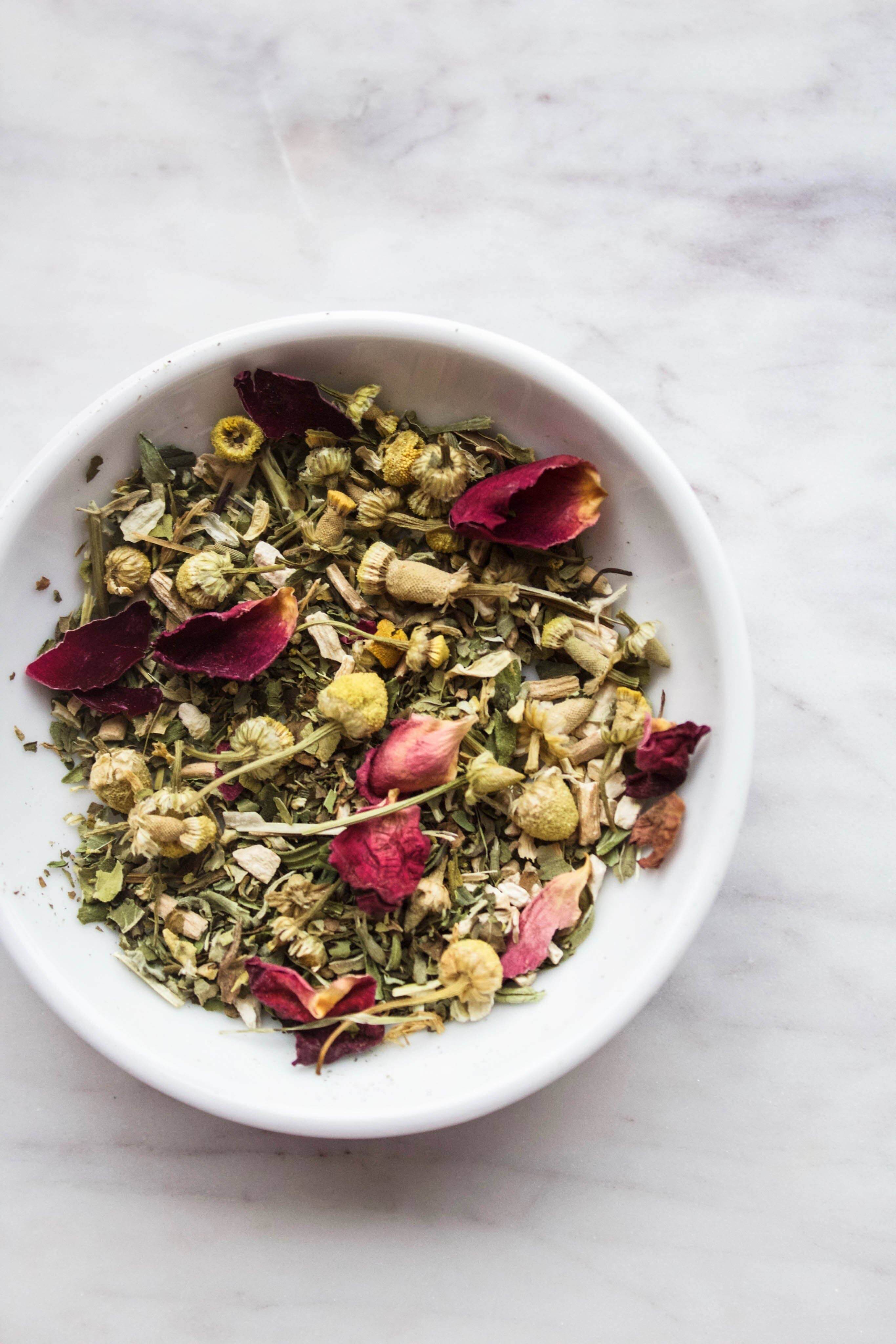 Organic herbal tea blend with chamomile, peppermint, and rose petals in a white bowl.