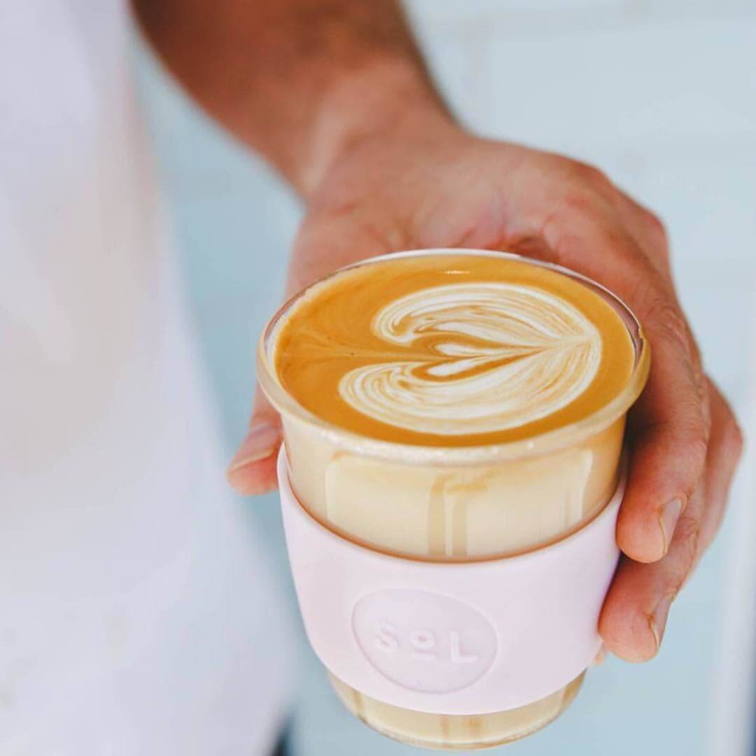 Hand holding a 12oz Perfect Pink glass travel tumbler with latte art, showcasing SOL Cups' sustainable design.