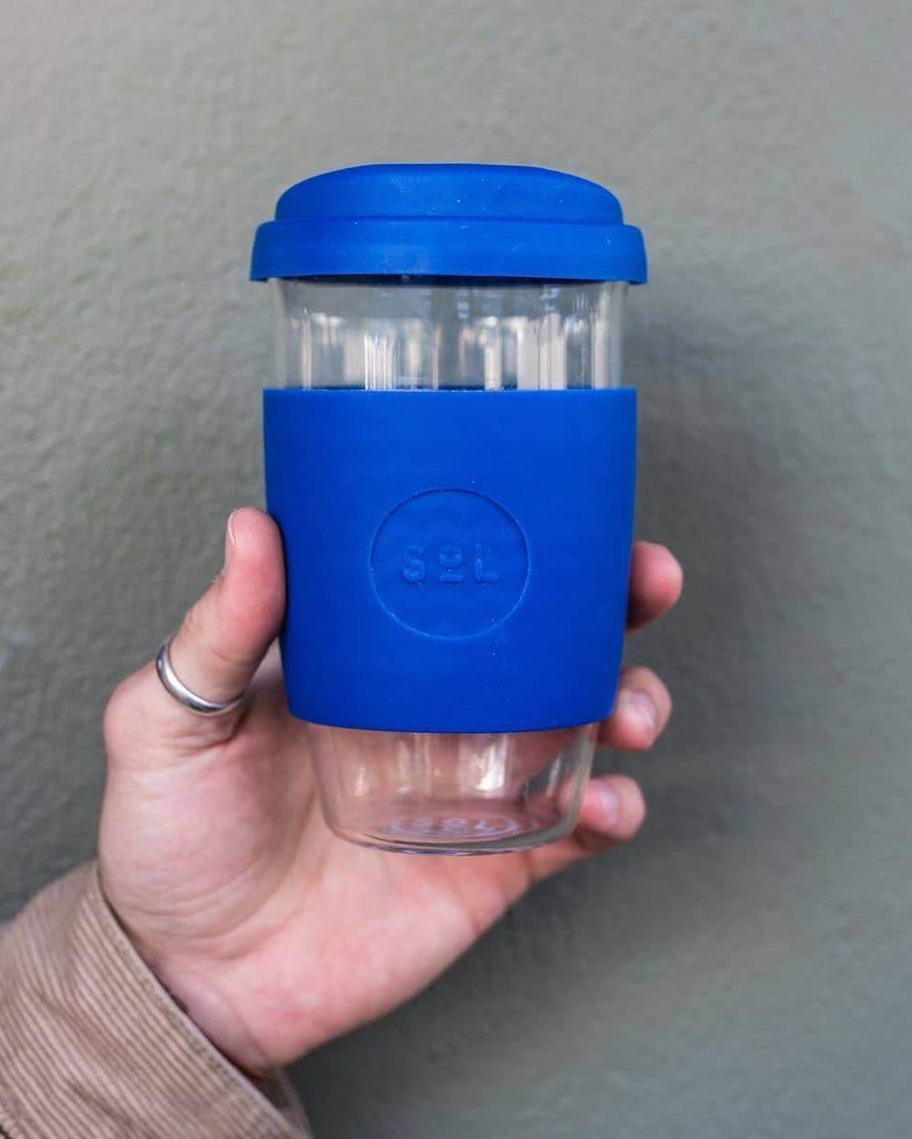 Hand holding a 16oz Winter Bondi Blue glass tumbler with silicone sleeve from SOL Cups.