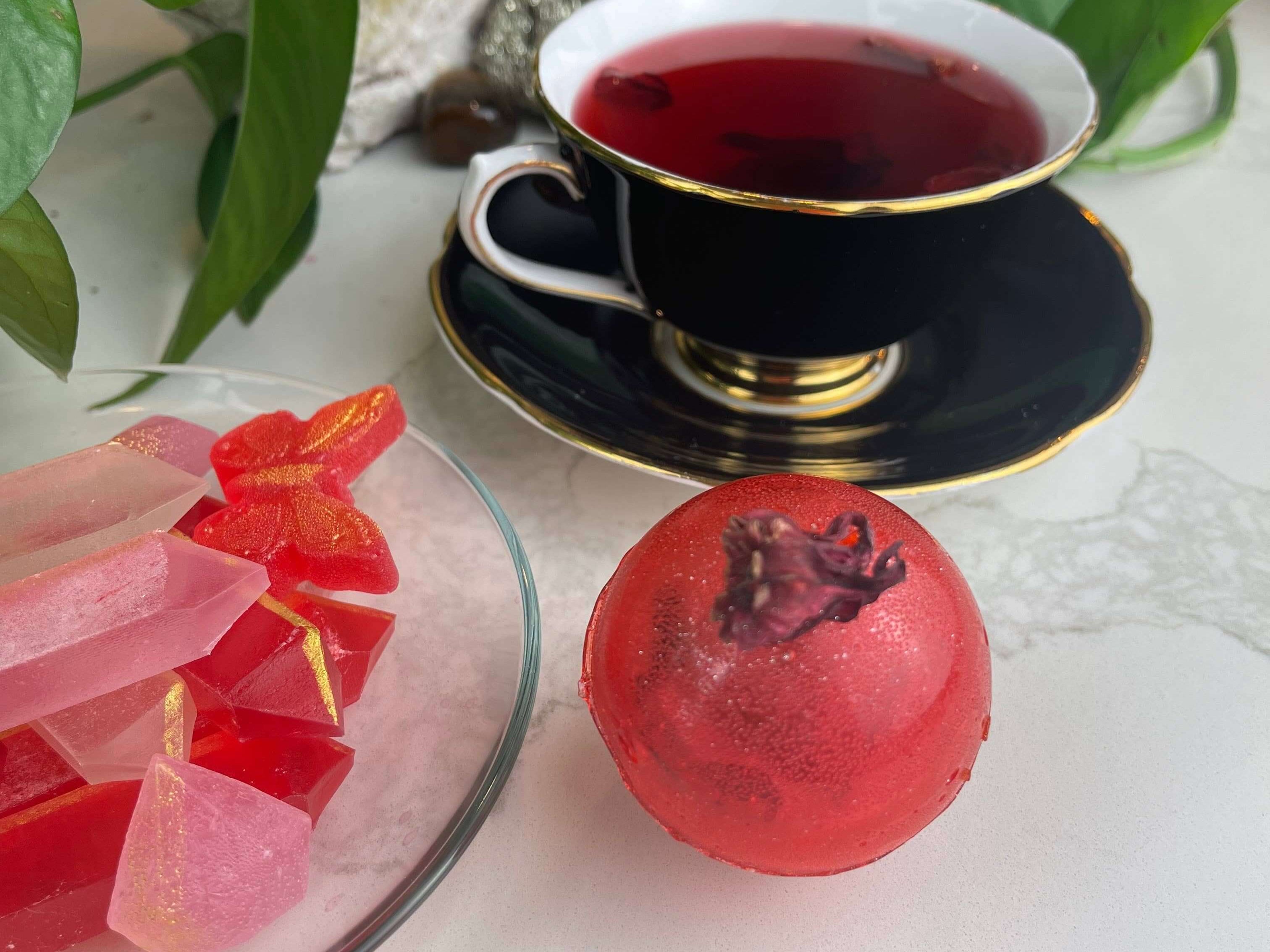 Berry Hibiscus Tea Bomb with a cup of tea and colorful treats, perfect for gifts and party favours.