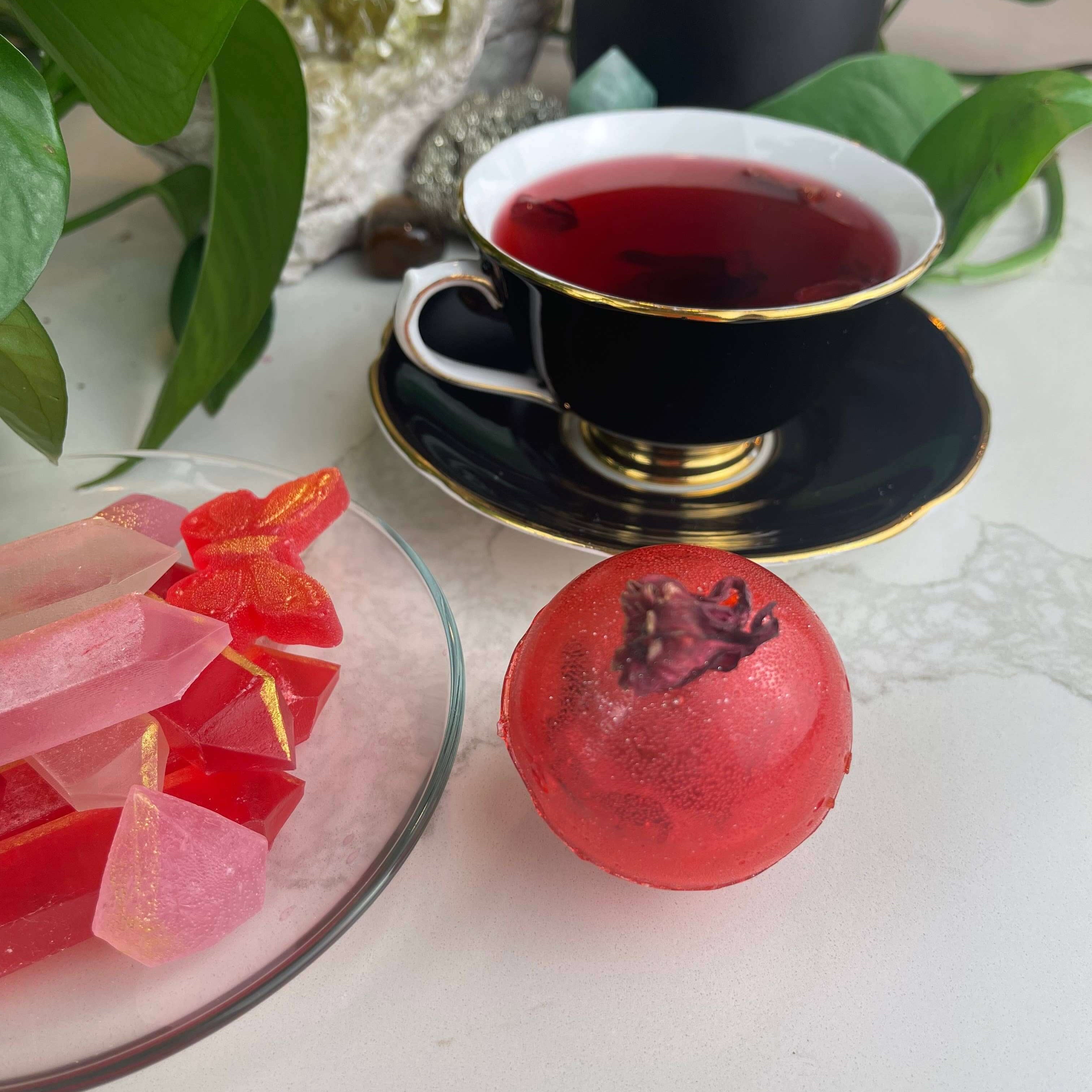 Berry Hibiscus Tea Bomb with a cup of tea and colorful treats, perfect for gifts and party favours.