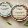 Two tins of balm labeled 'Balsam Salve' and 'Fire Balm' on a light background with green leaves.