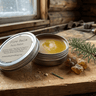 Two tins of Fire Balm Pain Salve on a wooden surface with a sprig of pine and resin.