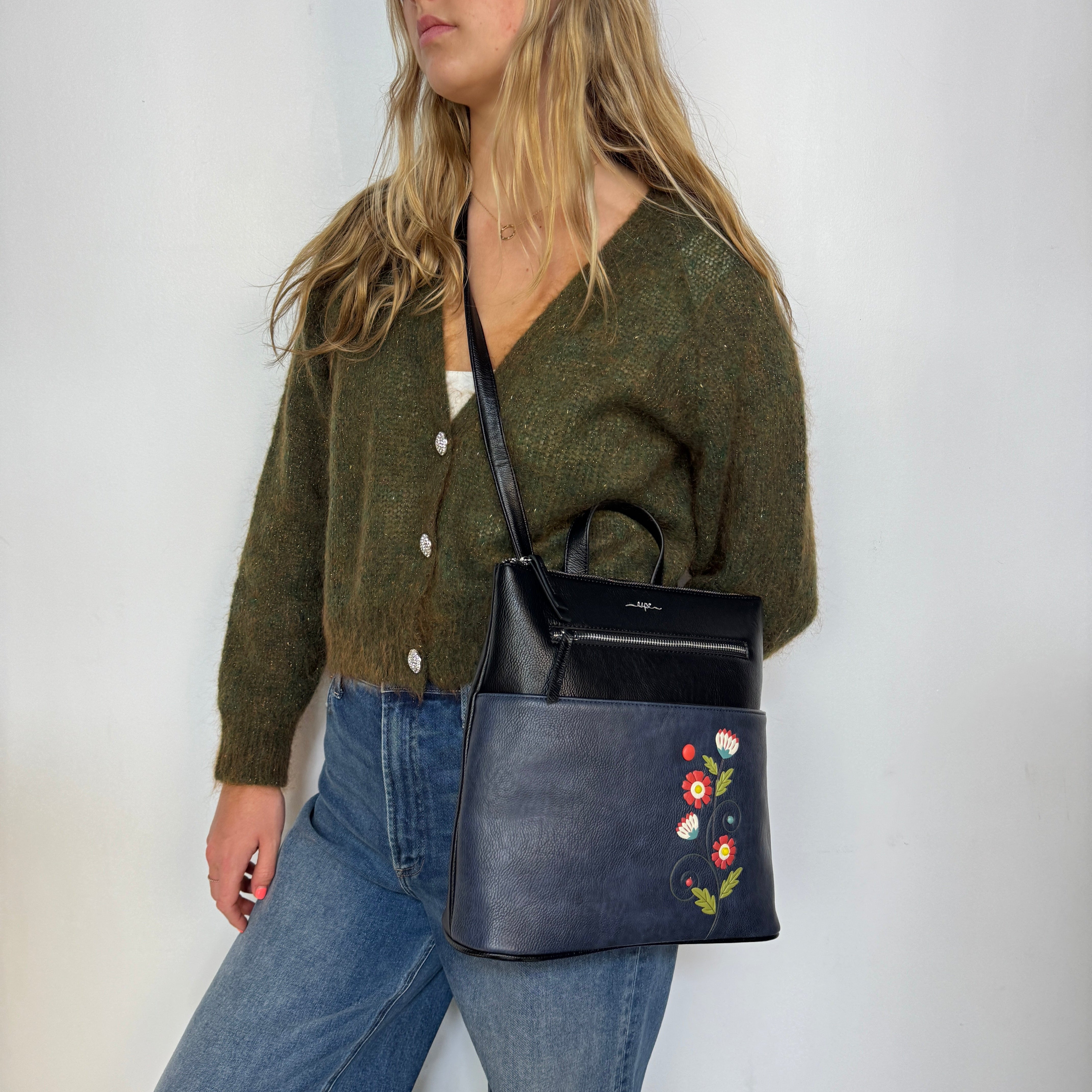 Woman holding a Espe Vegan Corp navy blue handbag with floral embroidery against a white background