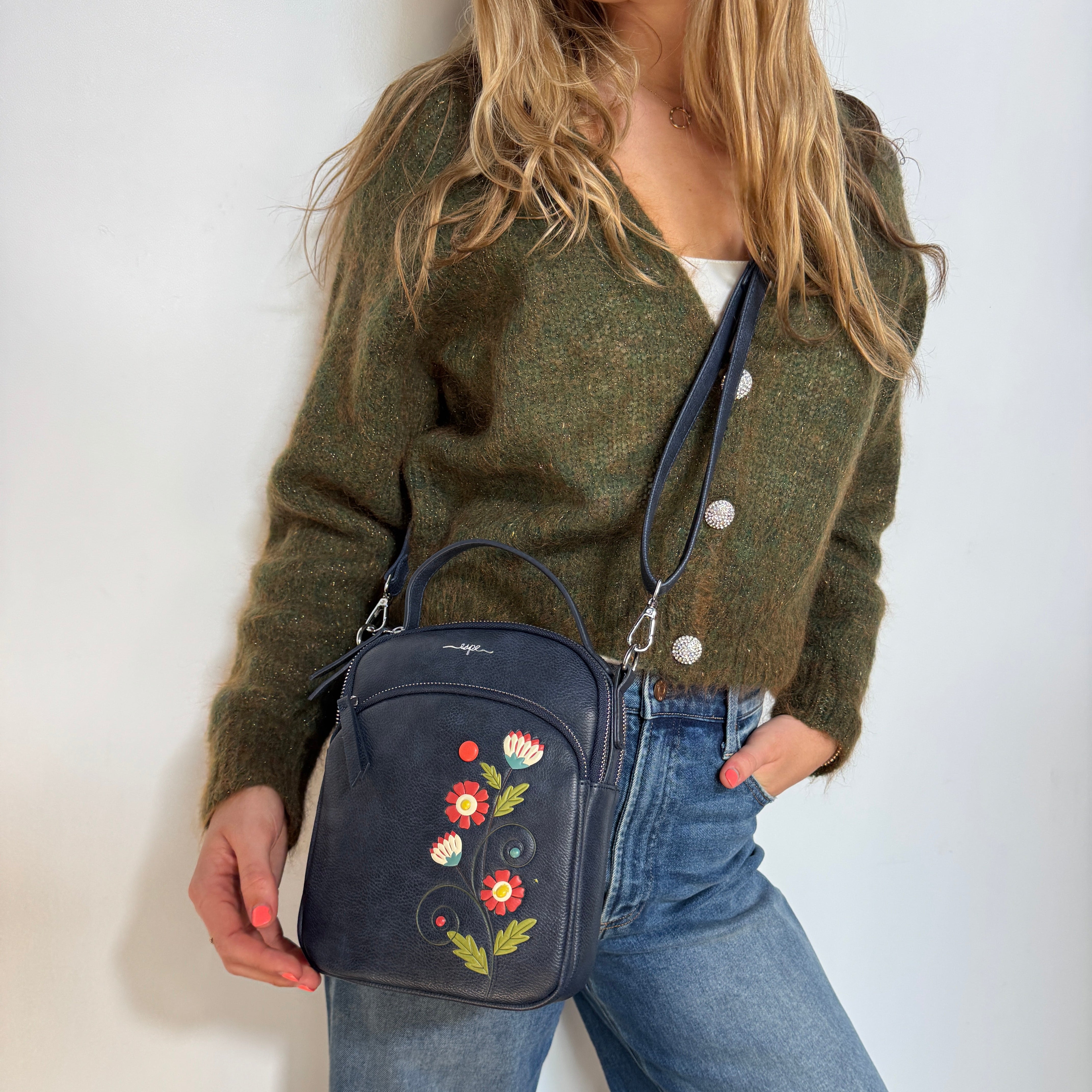 Person wearing a green sweater and blue jeans holding a Espe Vegan Corp dark blue handbag with floral embroidery.