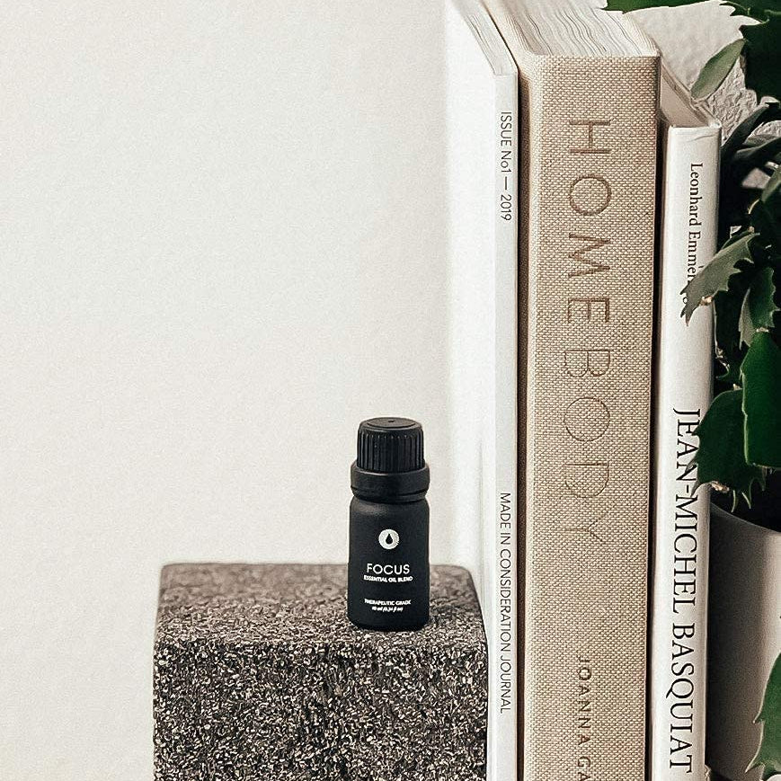 Small black bottle labeled 'FOCUS' on a textured surface with books and a plant in the background.
