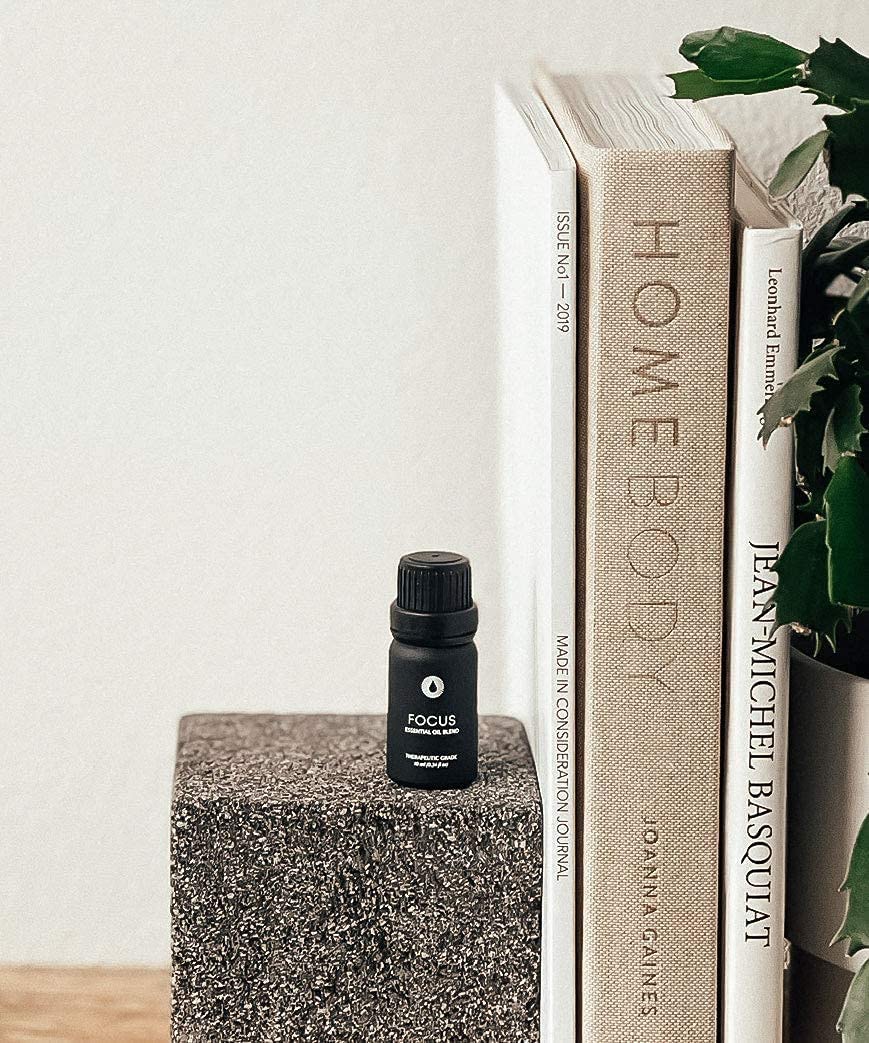 Small black bottle labeled 'FOCUS' on a textured surface with books and a plant in the background.