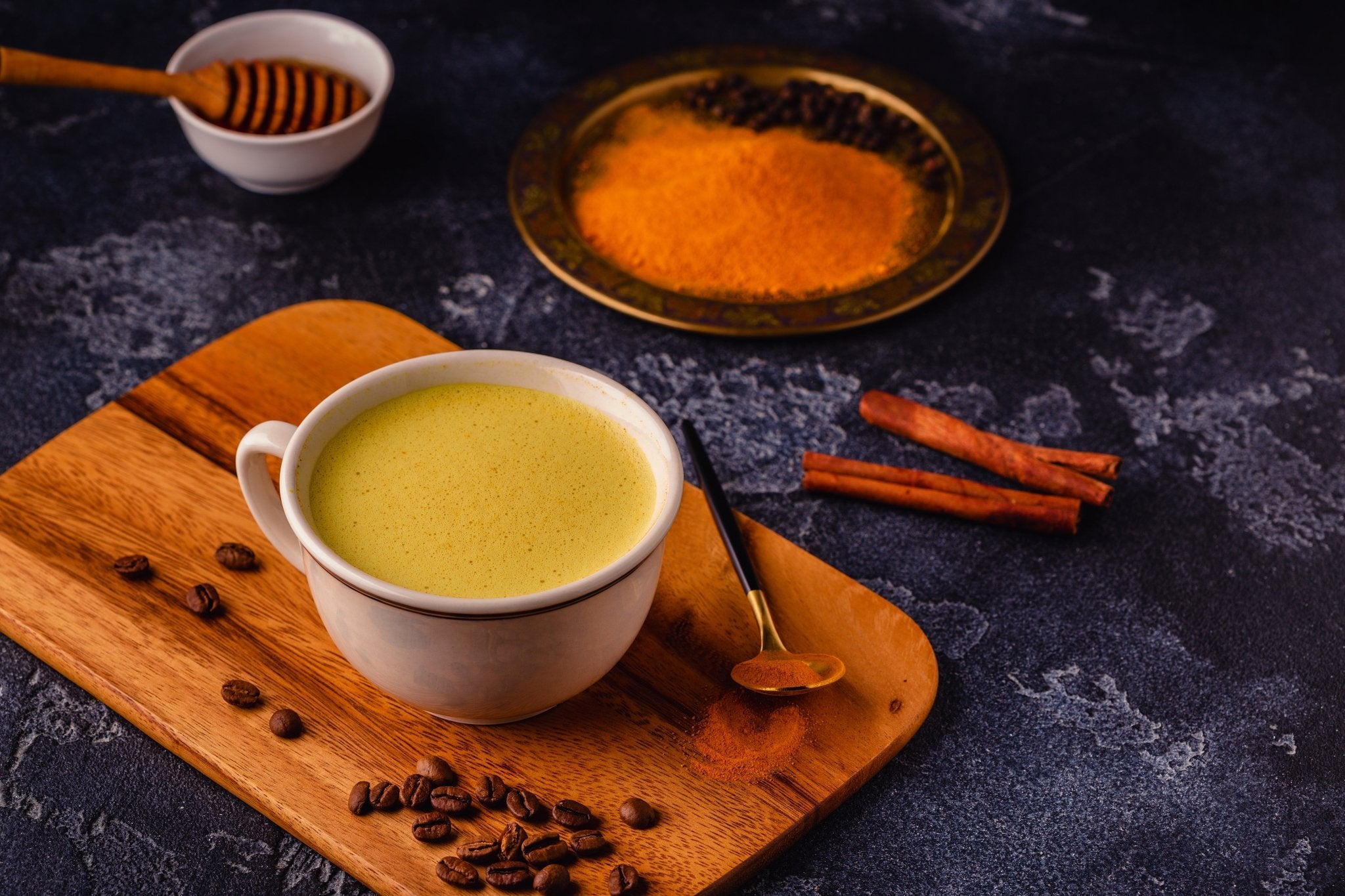 Cup of green tea with milk on a wooden board with spices and coffee beans on a dark background