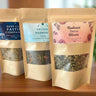 Kootenay Woman Three tea packages with labels on a wooden surface