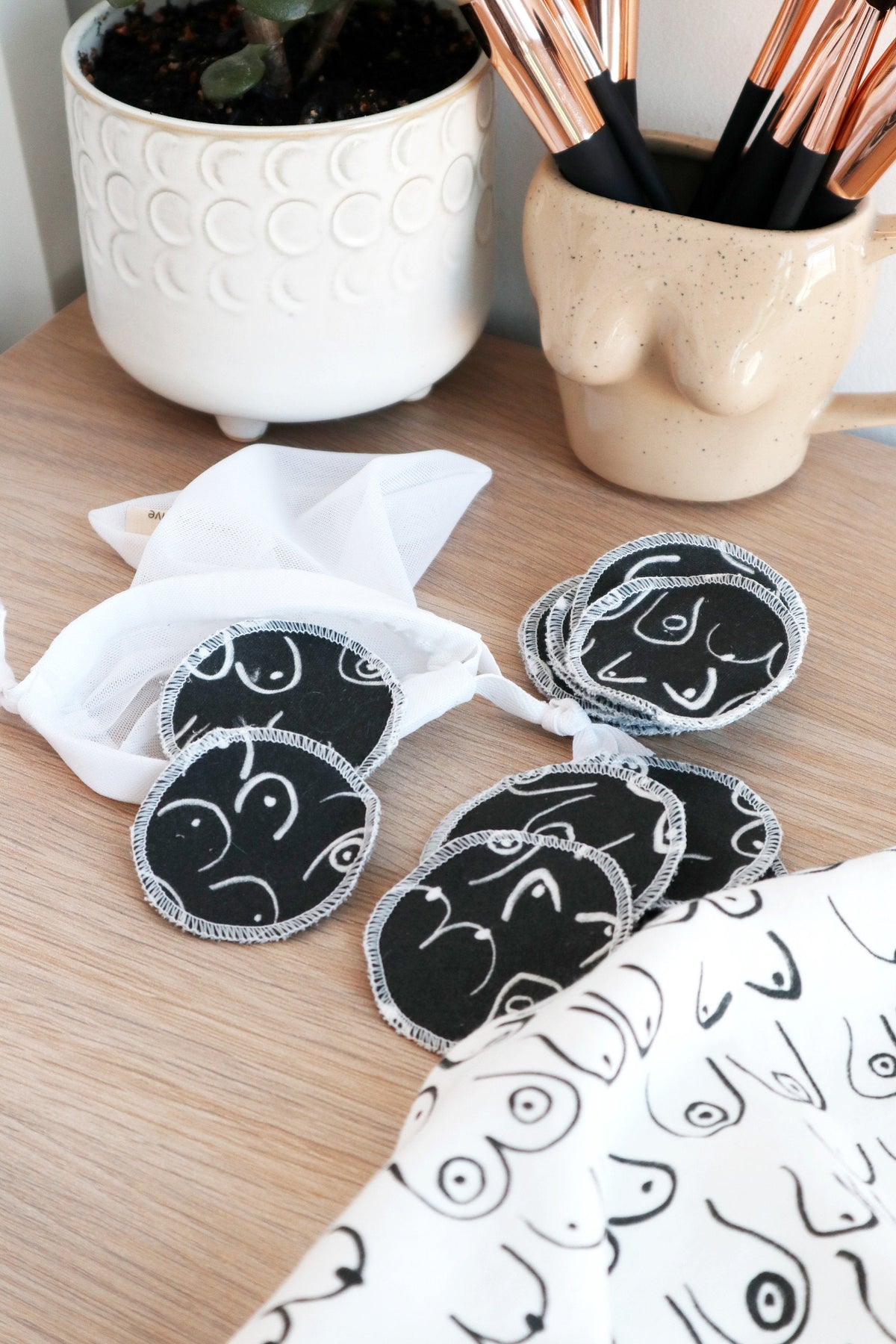 Black and white resuable cotton makeup pads on a white cloth by Freon Collective with makeup brushes