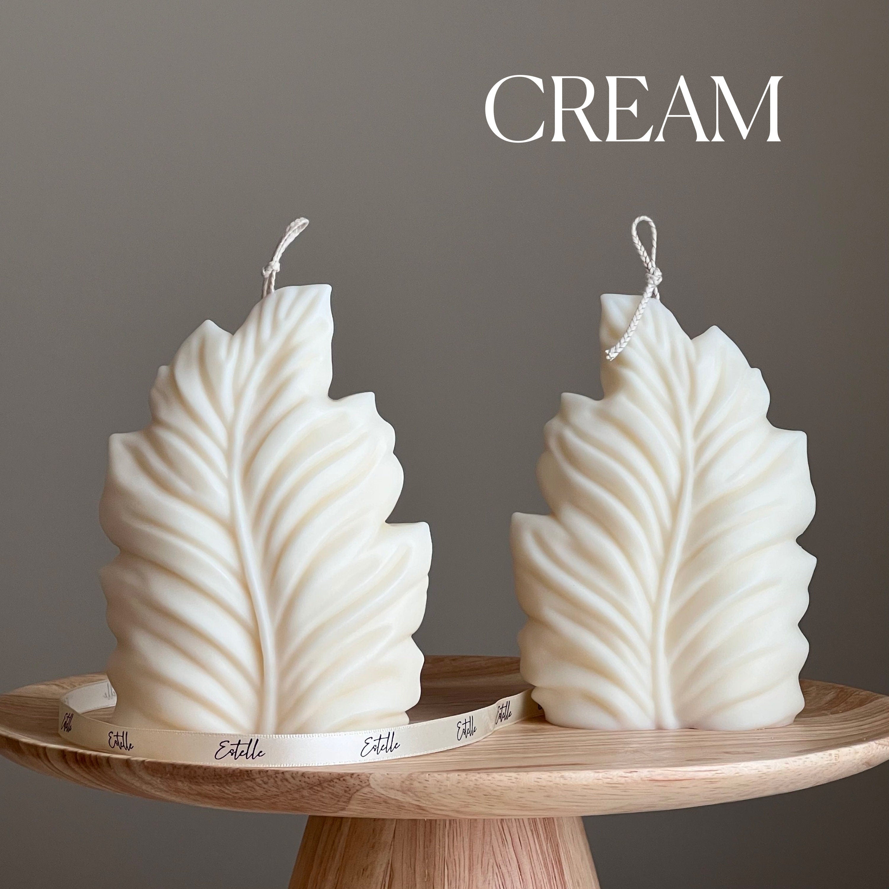 Two leaf-shaped candles on a wooden stand with 'CREAM' text above.
