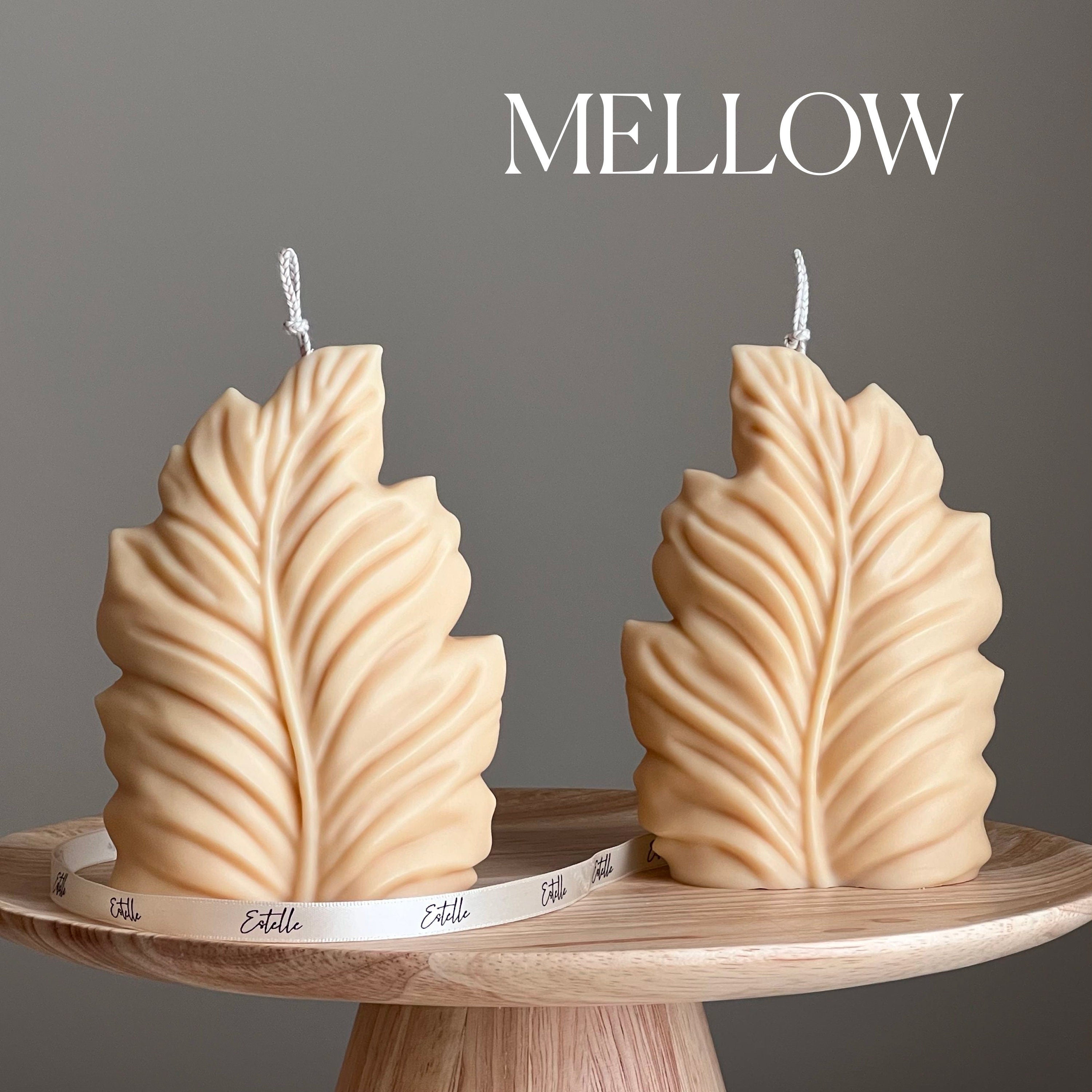 Two leaf-shaped candles on a wooden stand with 'MELLOW' branding against a gray background.