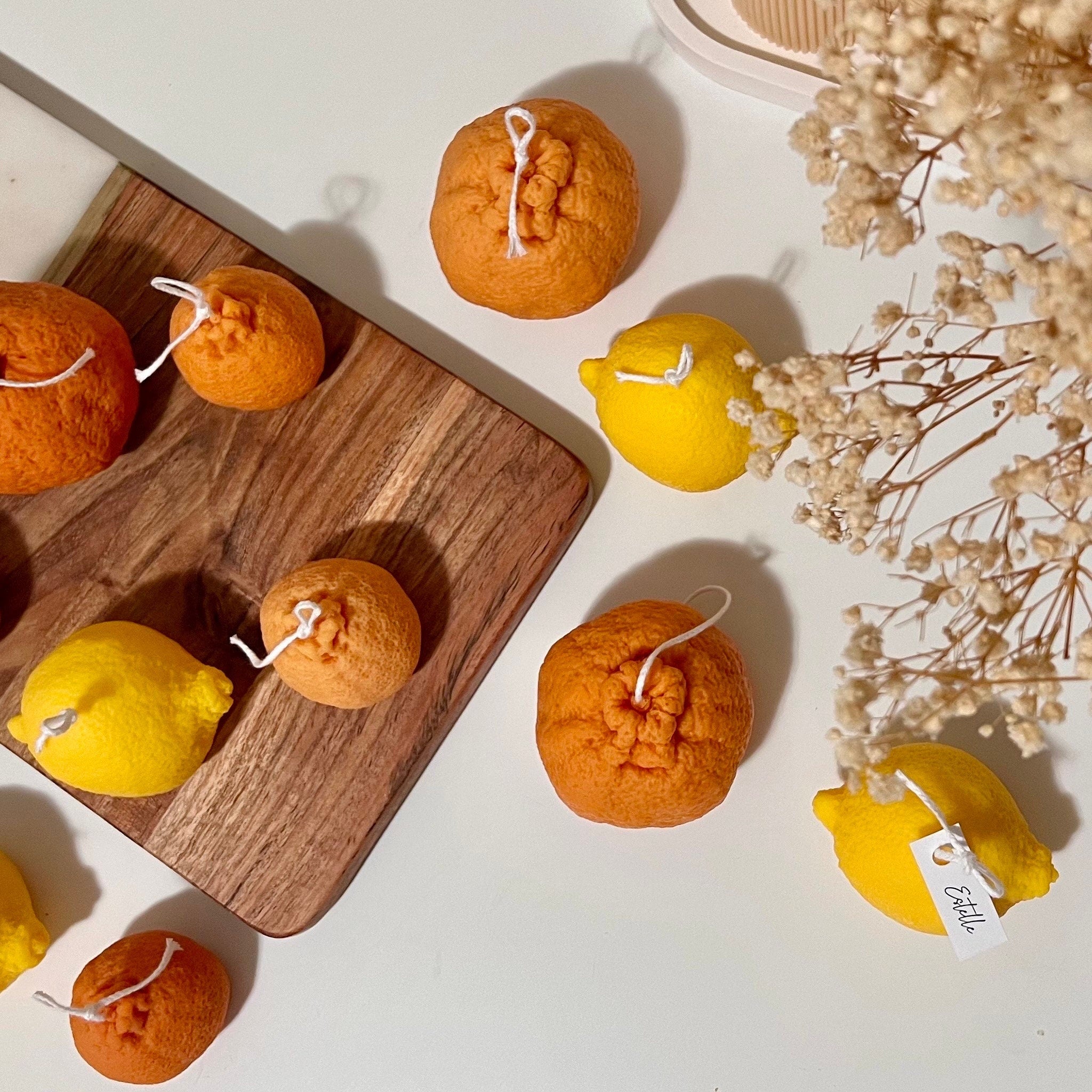 Decorative candles shaped like lemons and oranges on a wooden board with dried flowers.