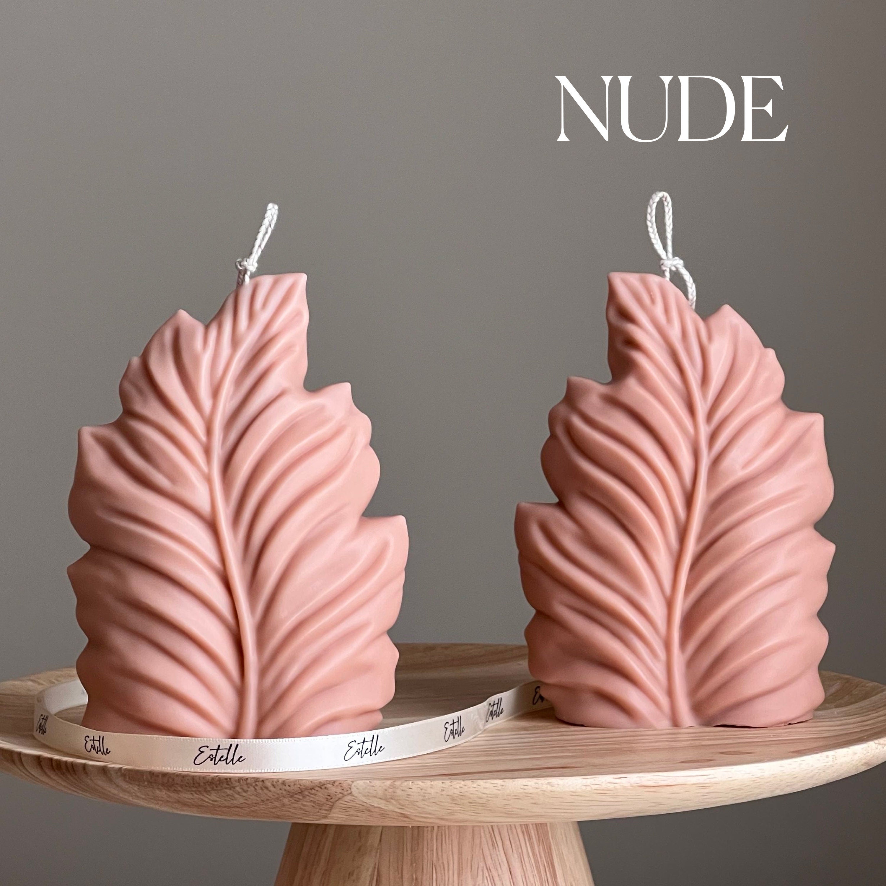 Two pink leaf-shaped candles on a wooden stand with 'NUDE' text above.