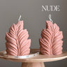 Two pink leaf-shaped candles on a wooden stand with 'NUDE' text above.