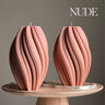Two pink textured candles on a wooden stand with 'NUDE' text above.