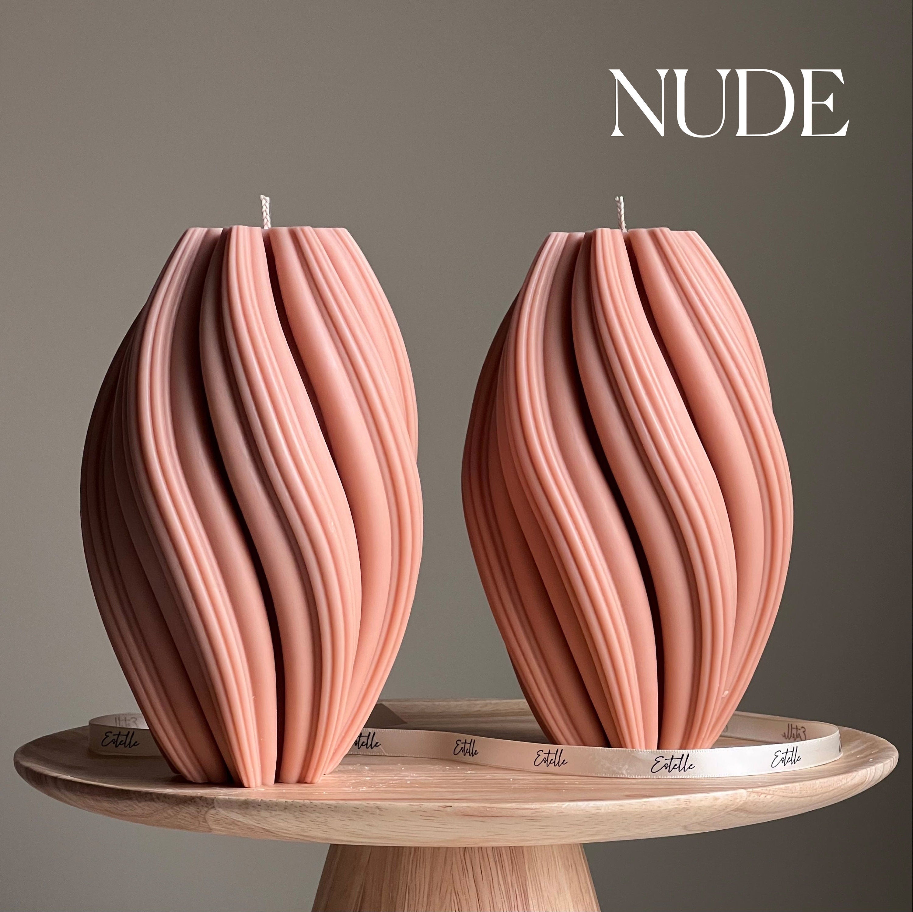 Two pink textured candles on a wooden stand with 'NUDE' text above.