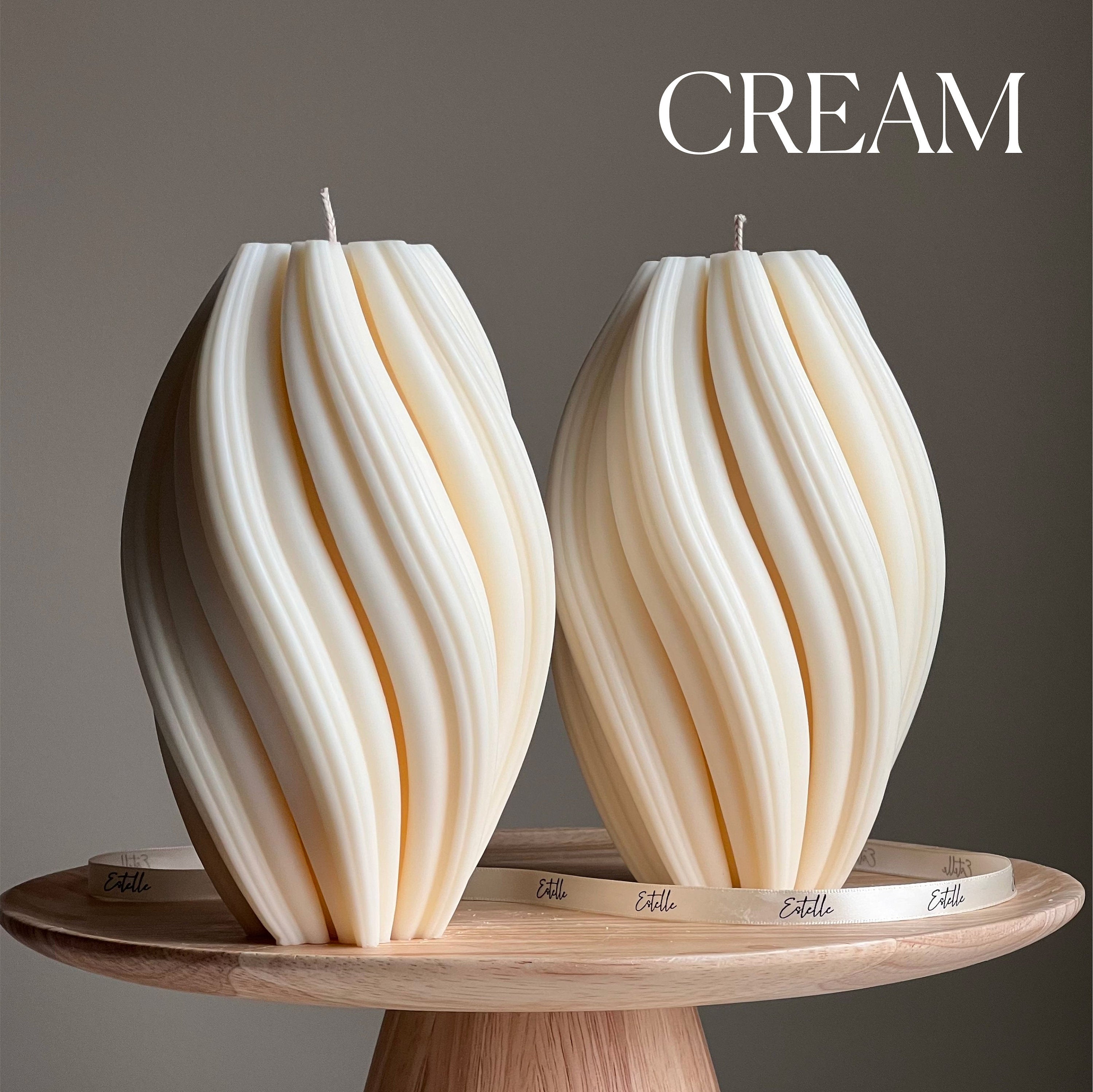 Two cream-colored candles with wicks on a wooden stand against a gray background.