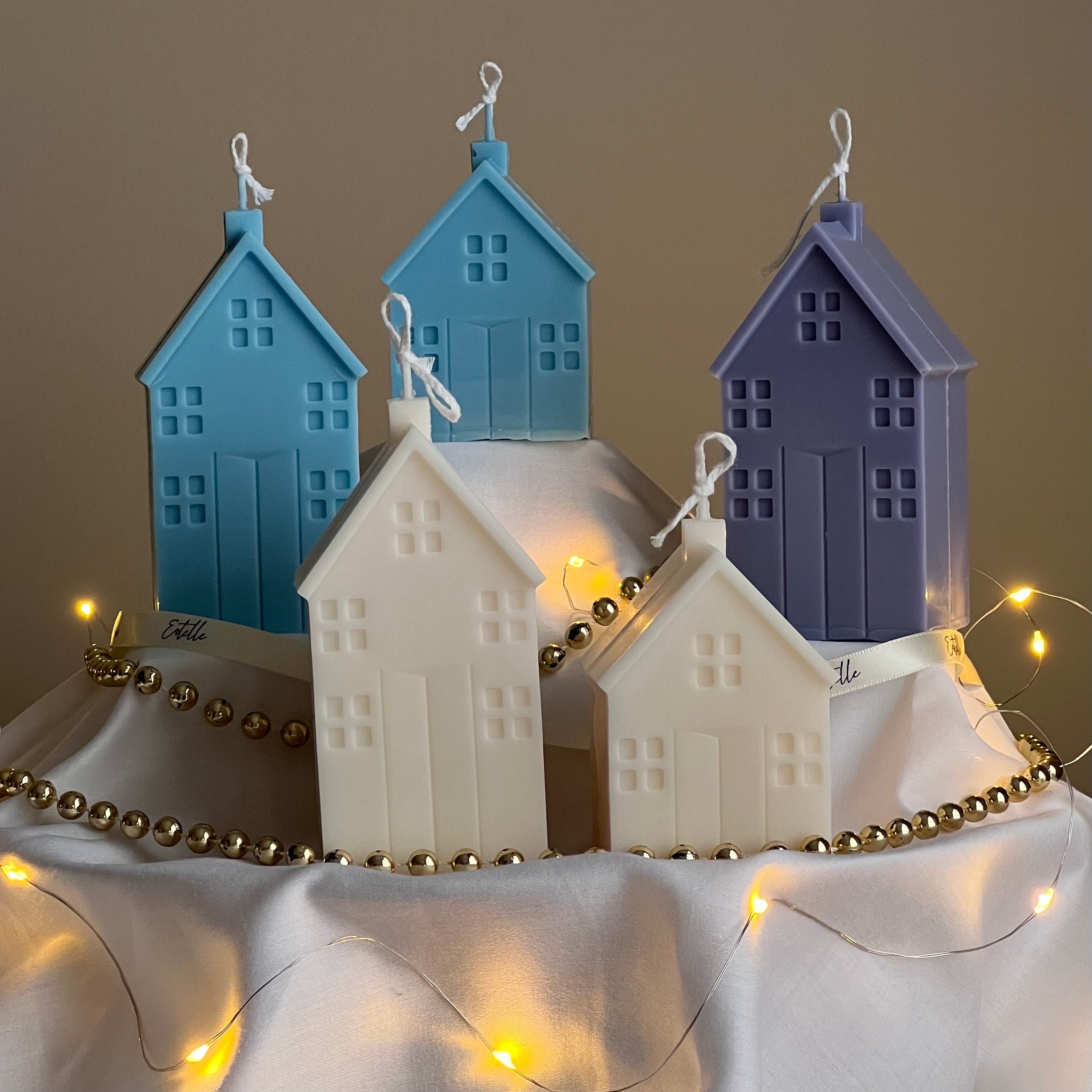 Decorative house-shaped candles with string lights on a neutral background