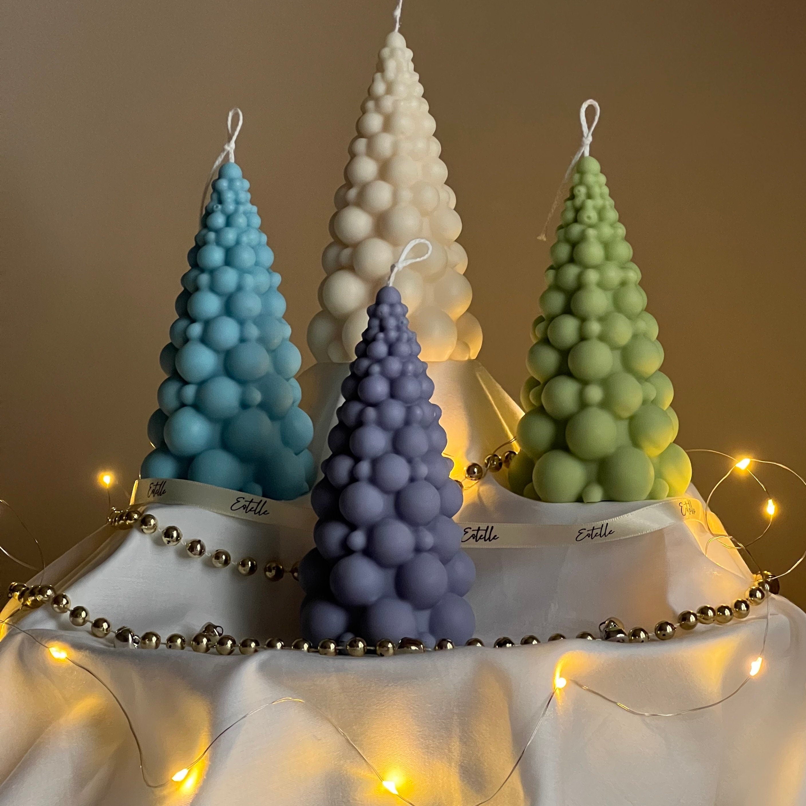 Four tree-shaped candles in blue, purple, and green on a stand with string lights.