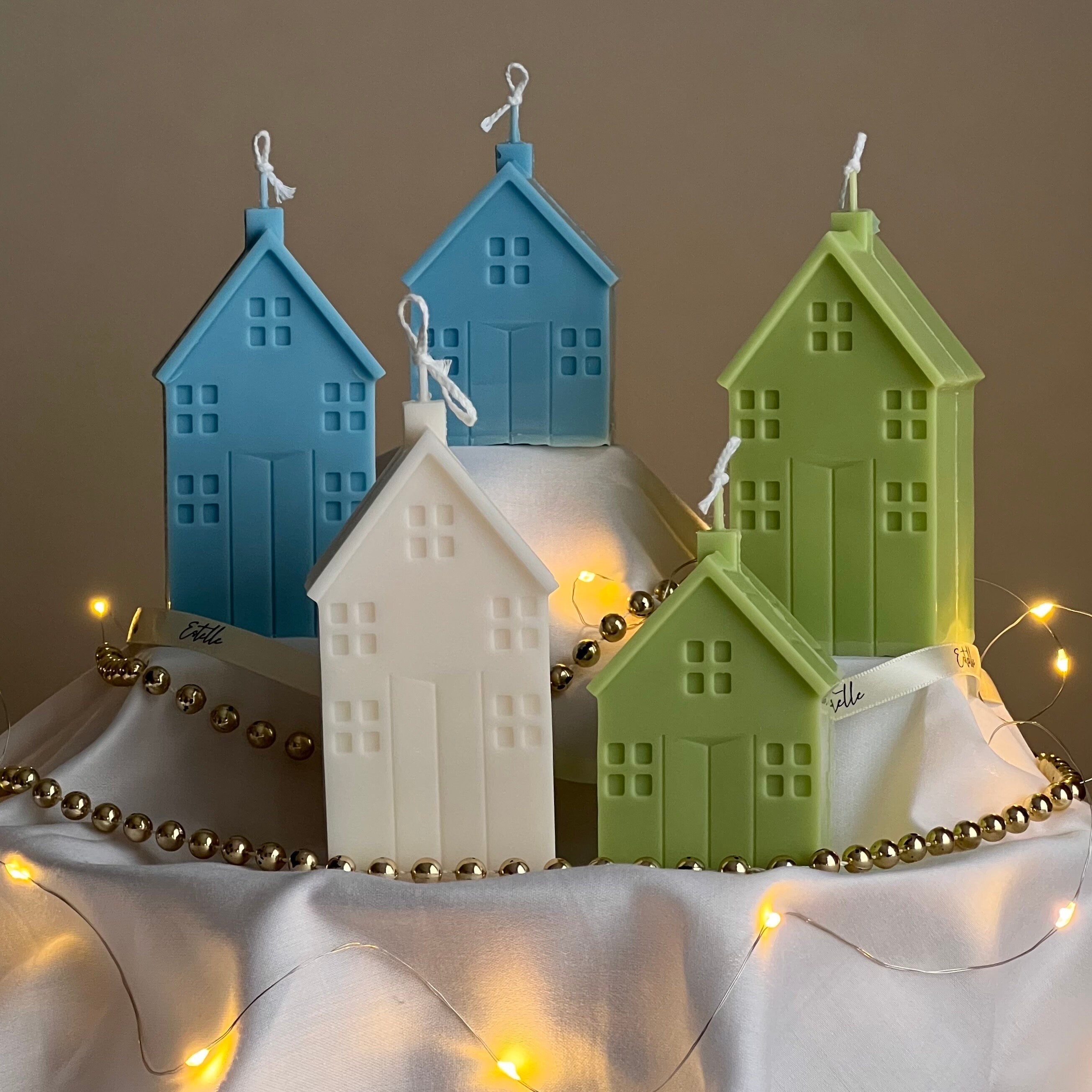 Set of colorful house-shaped candles with string lights on a neutral background
