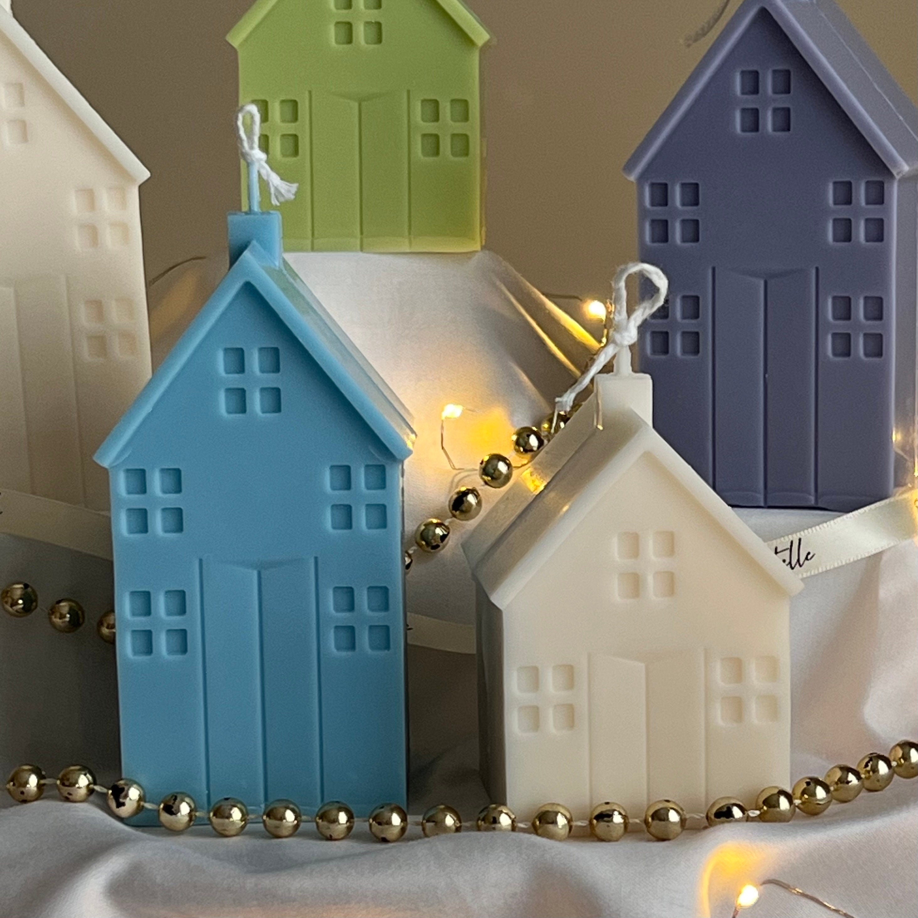 Decorative house-shaped candles with string lights on a neutral background