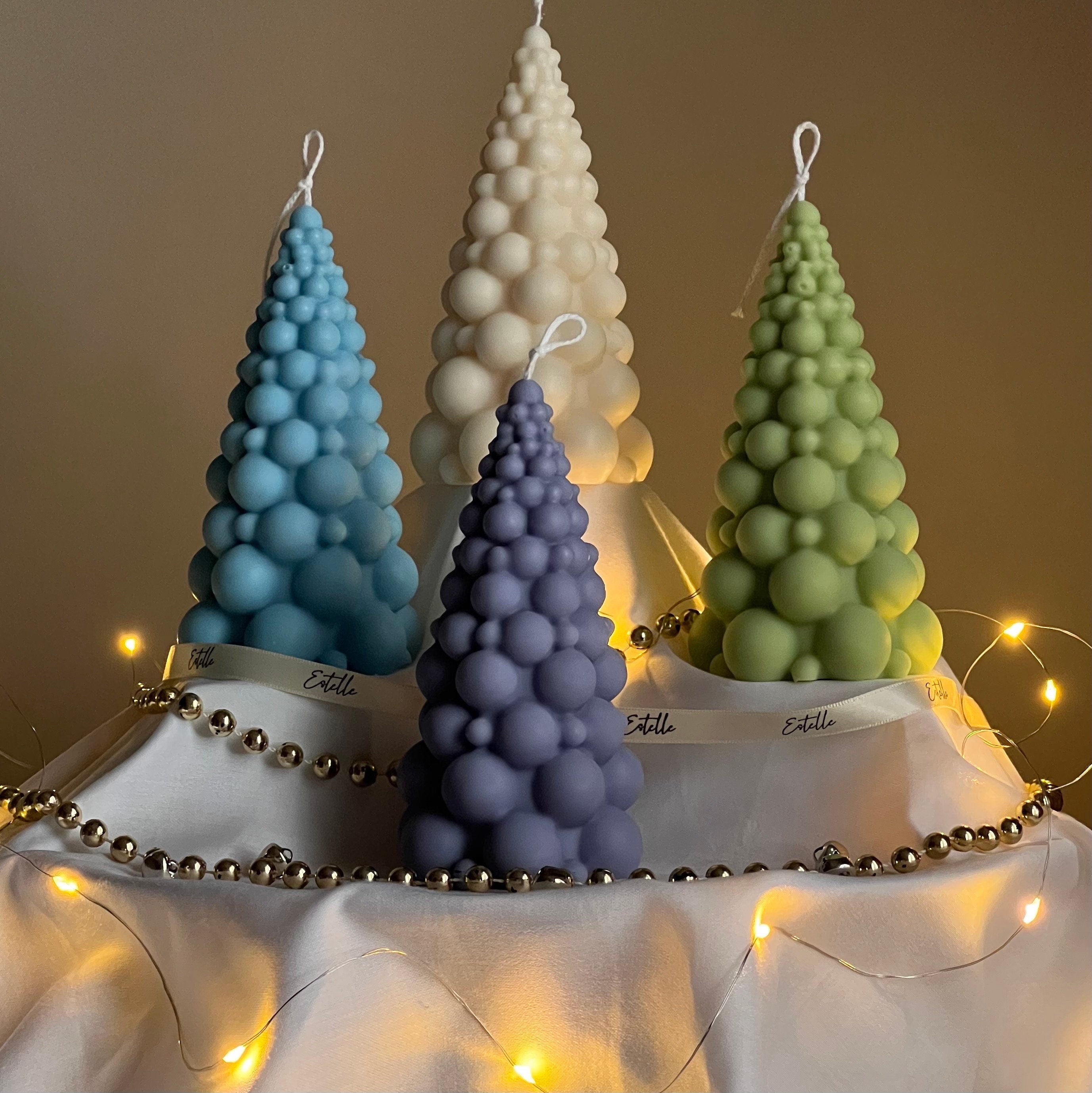Four bubble-textured candles in blue, purple, white, and green on a stand with string lights.