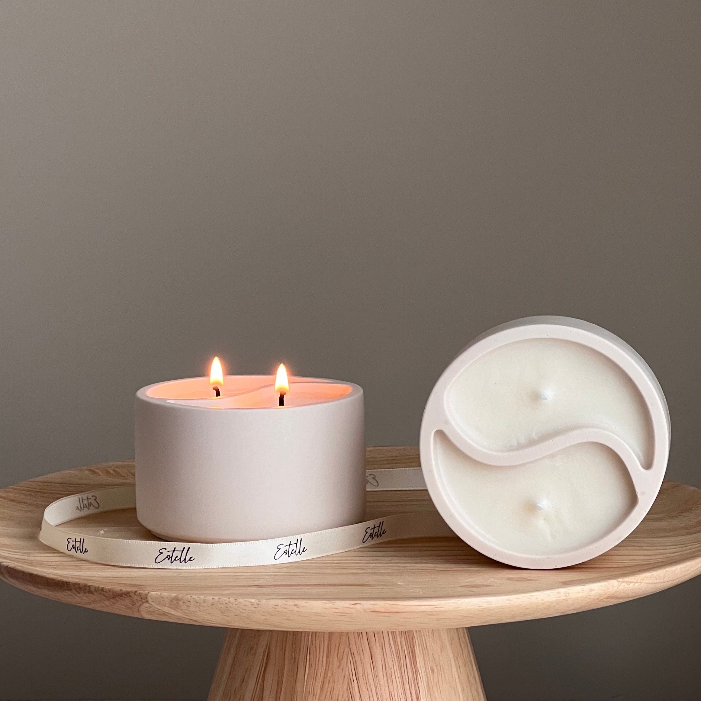 Two candles, one lit and one unlit, on a wooden surface with a neutral background.