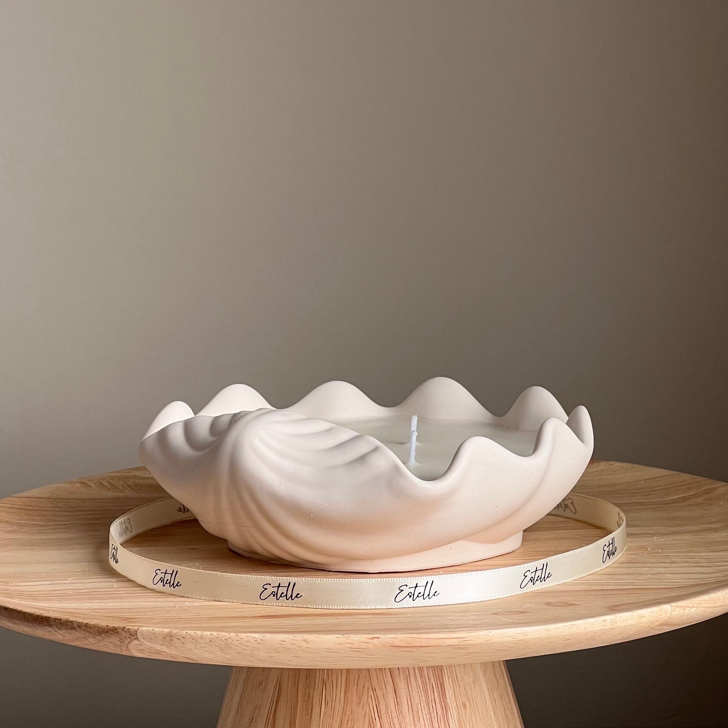 White ceramic shell-shaped bowl on a wooden stand with 'Estelle' branding against a plain background
