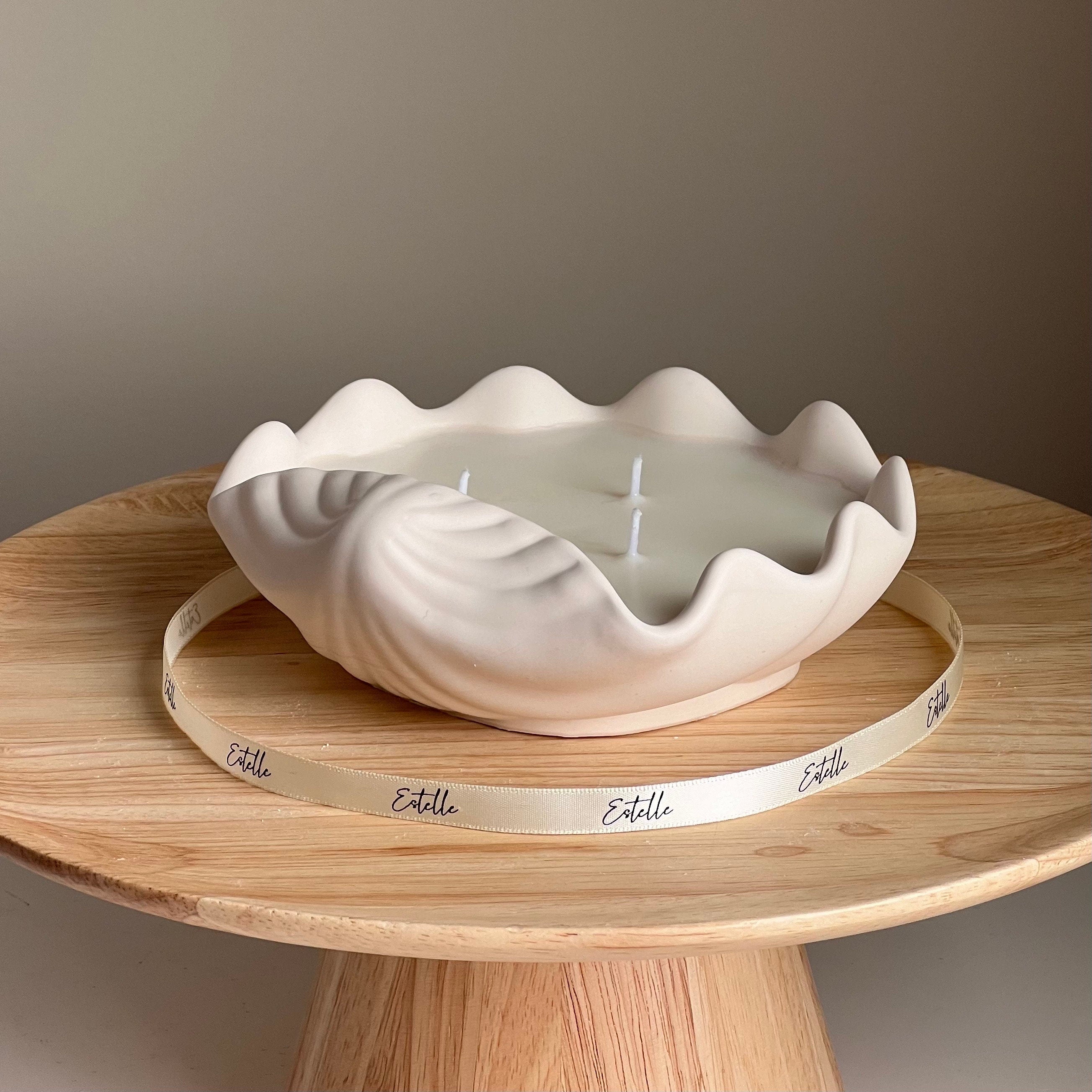 White shell-shaped candle on a wooden stand with 'Estelle' branding.