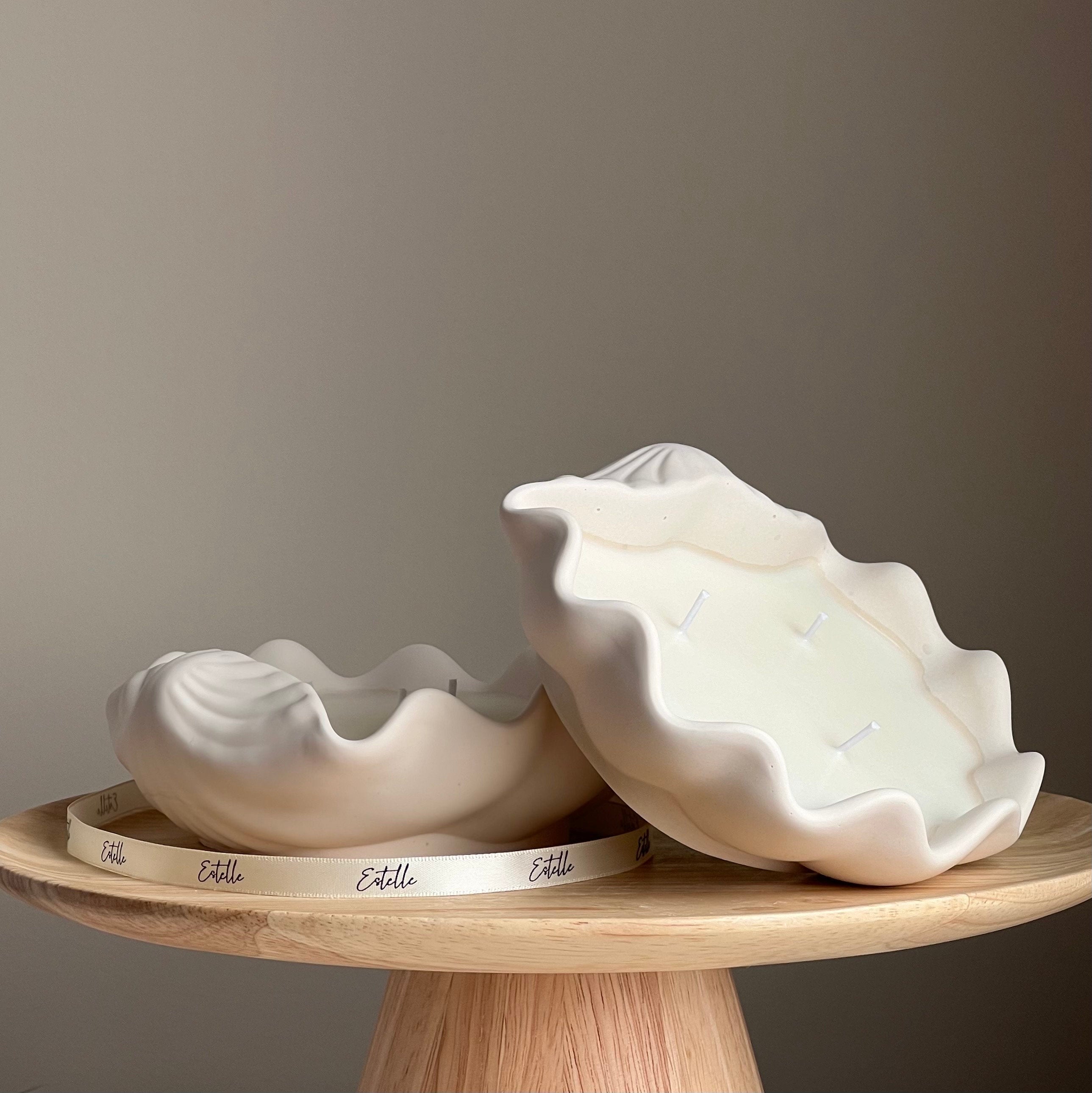 Two large ceramic shell-shaped bowls on a wooden stand with a neutral background
