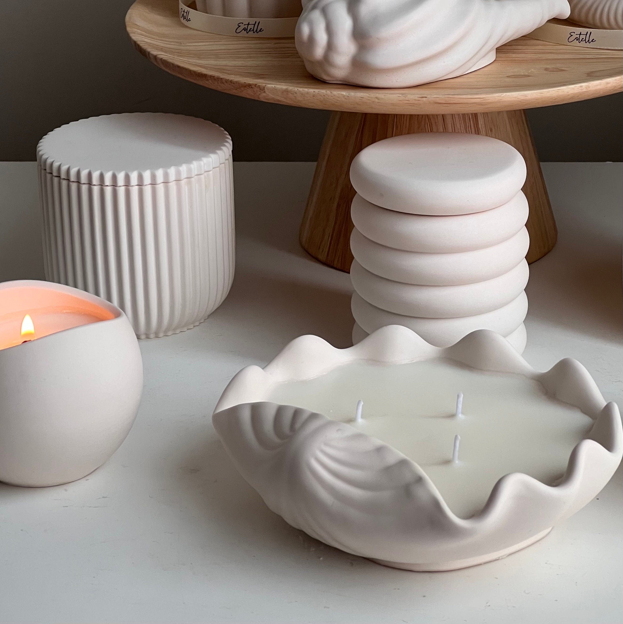 Ceramic shell-shaped candle holder with a lit candle on a white surface.