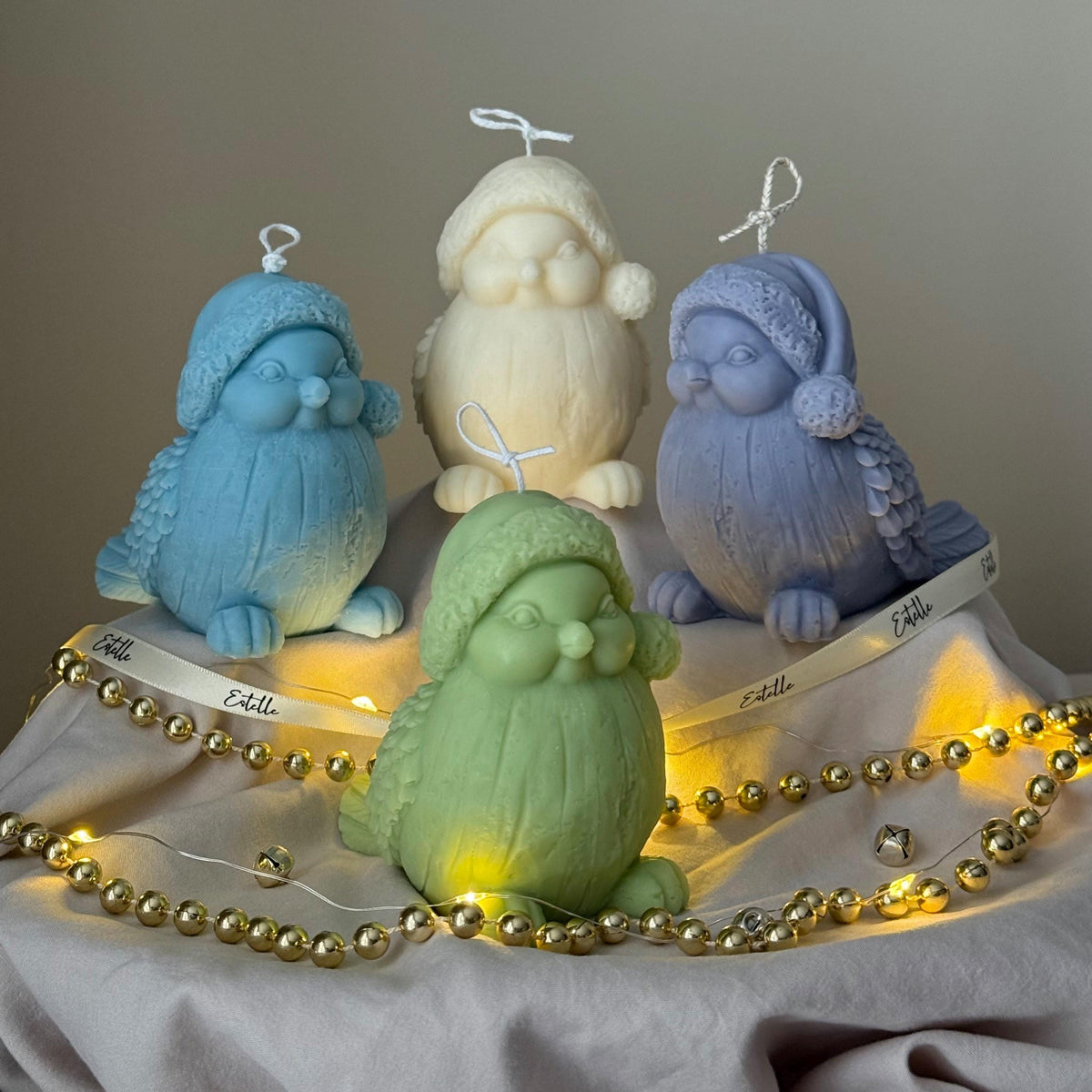 Four colorful bird-shaped candles on a wooden stand with string lights.