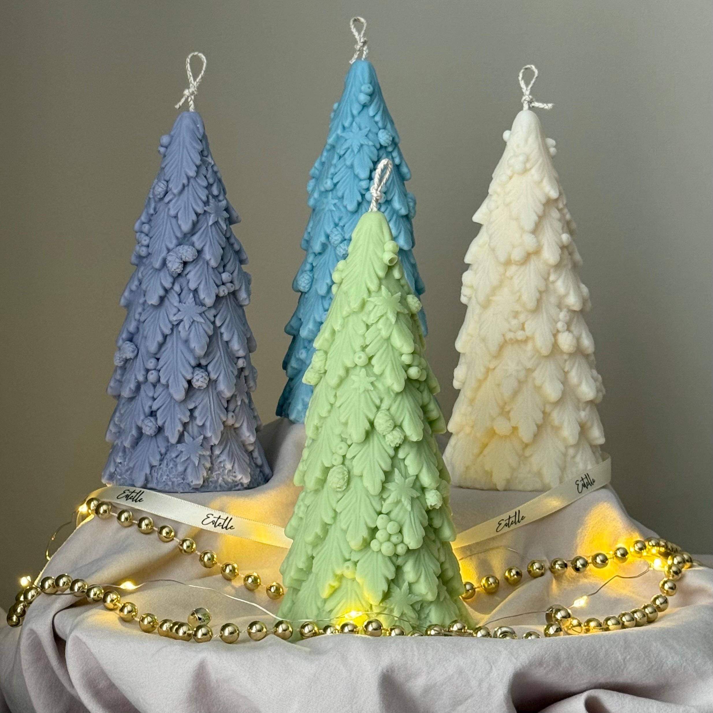Four tree-shaped candles in blue, green, and white on a gray surface with string lights.