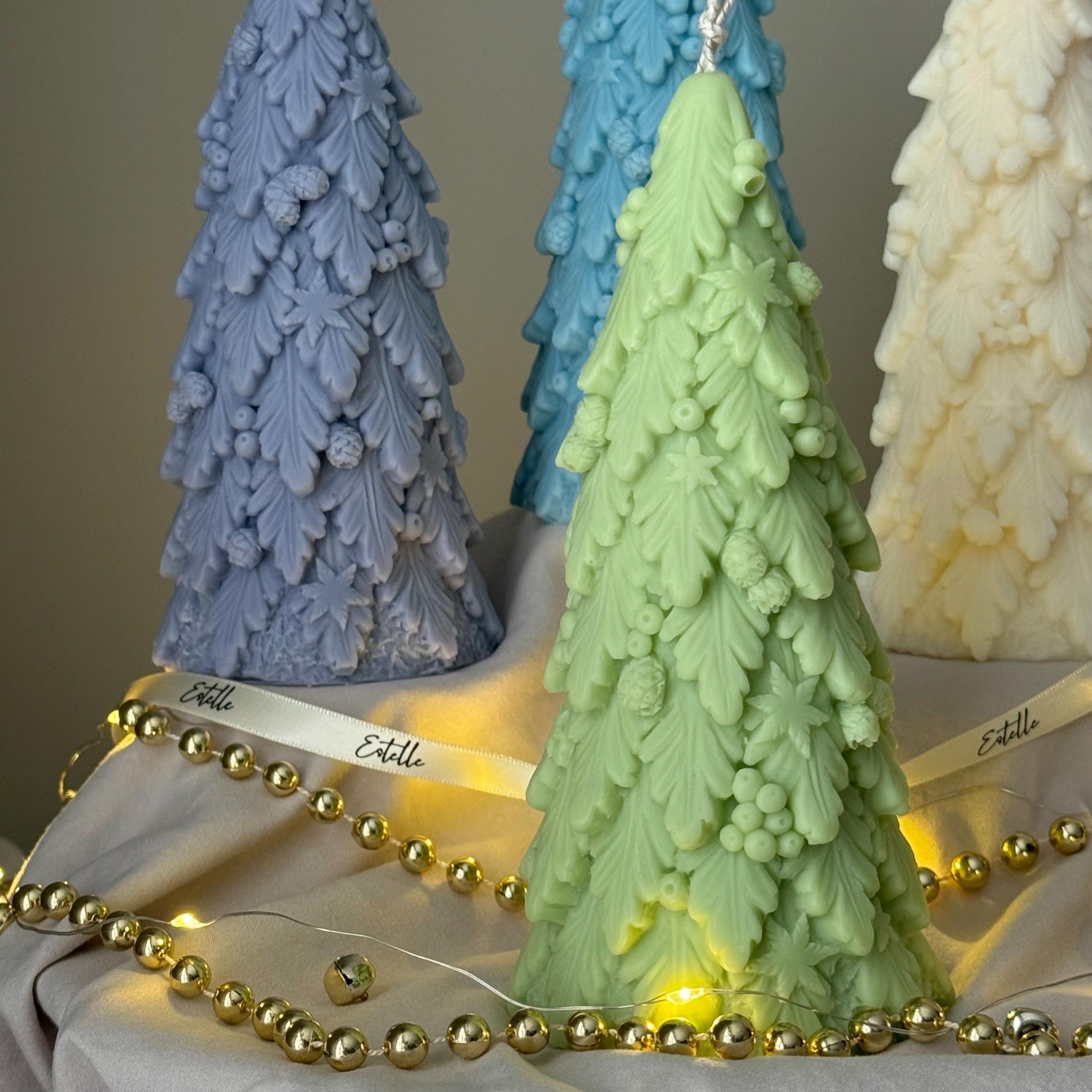 Three tree-shaped candles in blue, green, and white with gold beads and string lights.