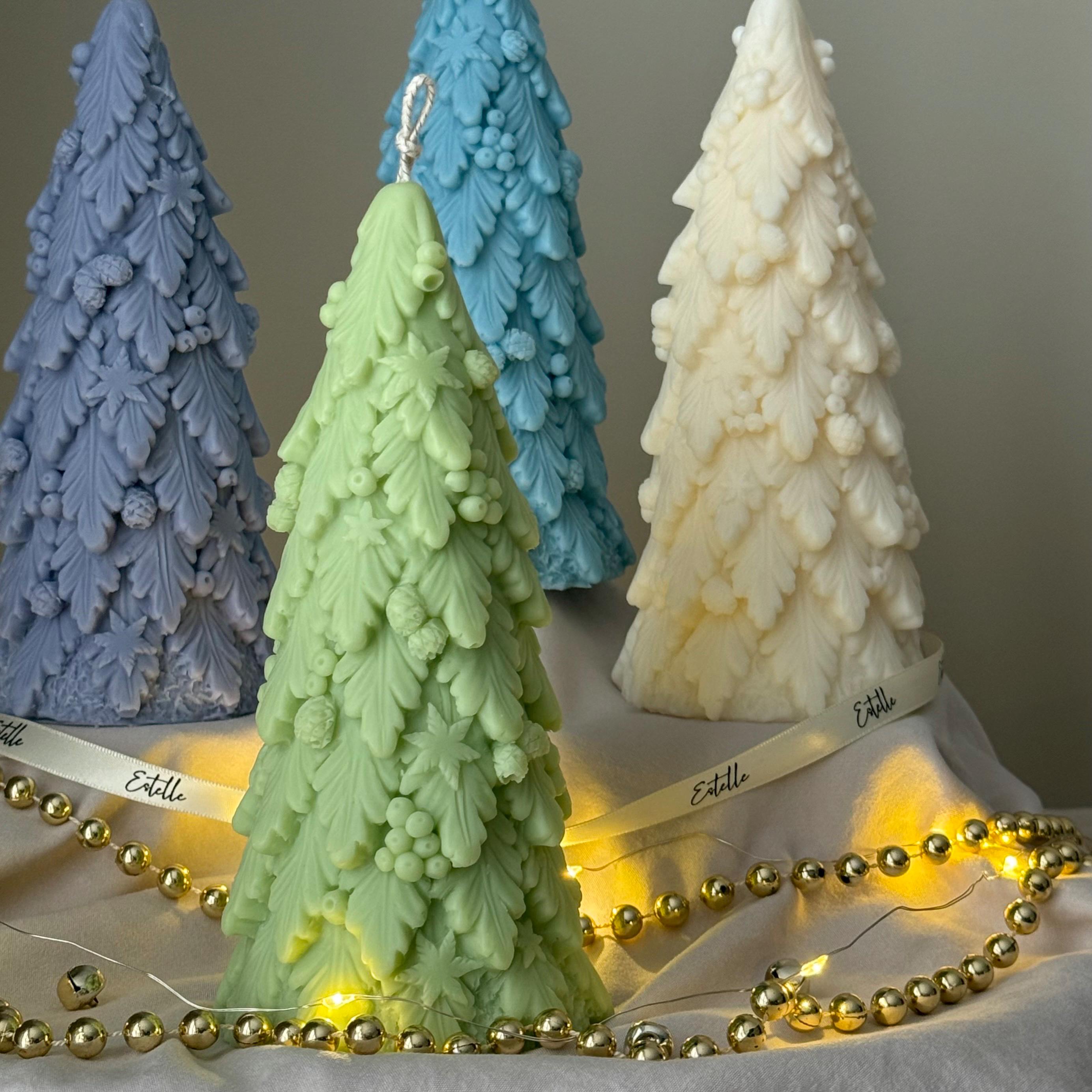 Three tree-shaped candles in blue, green, and white with string lights on a neutral background.