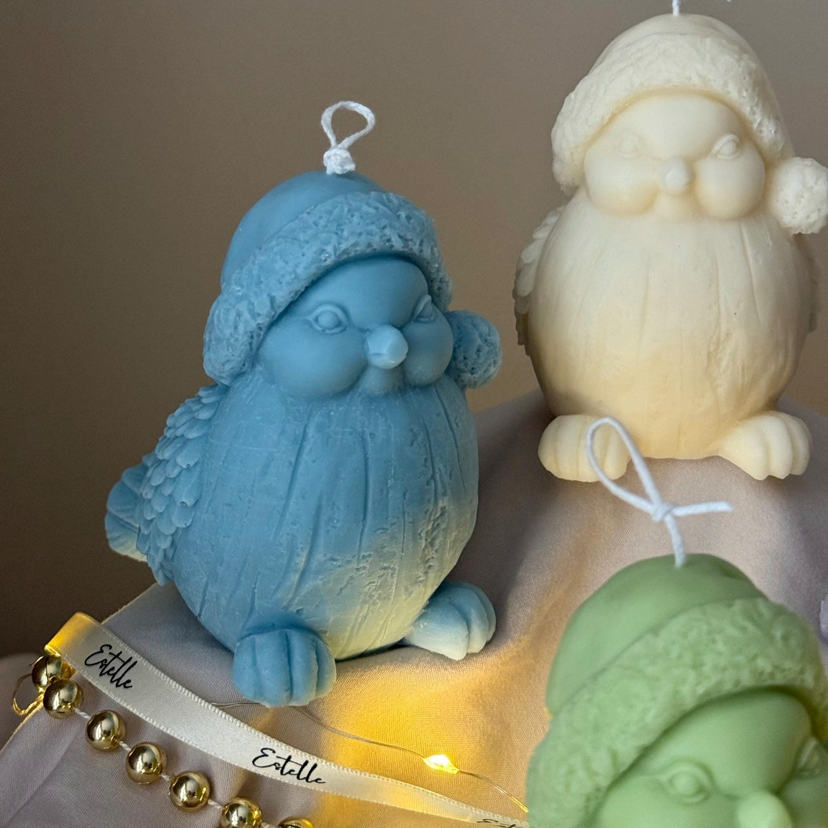 Four colorful bird-shaped candles on a wooden stand with string lights.