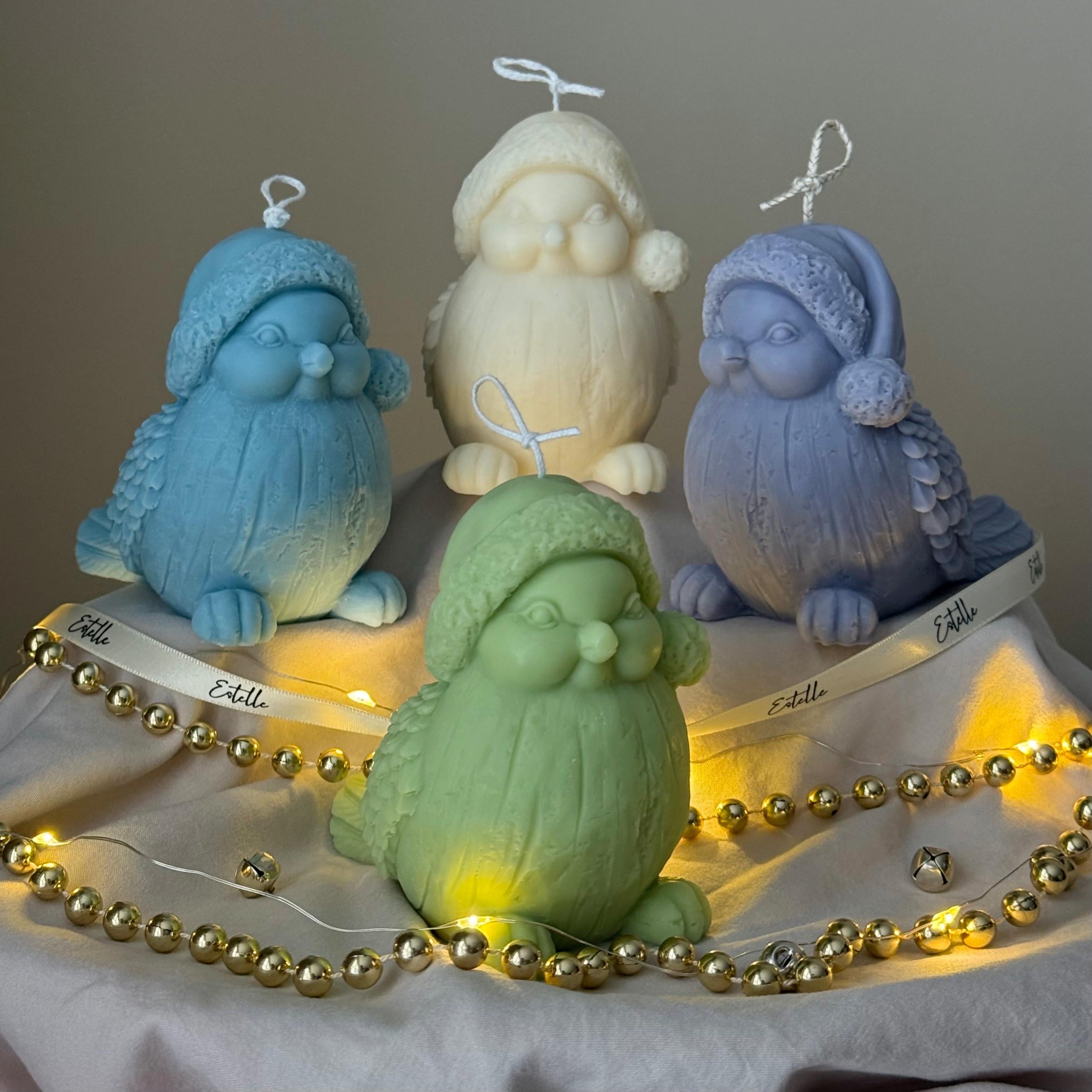 Four colorful bird-shaped candles on a wooden stand with string lights.