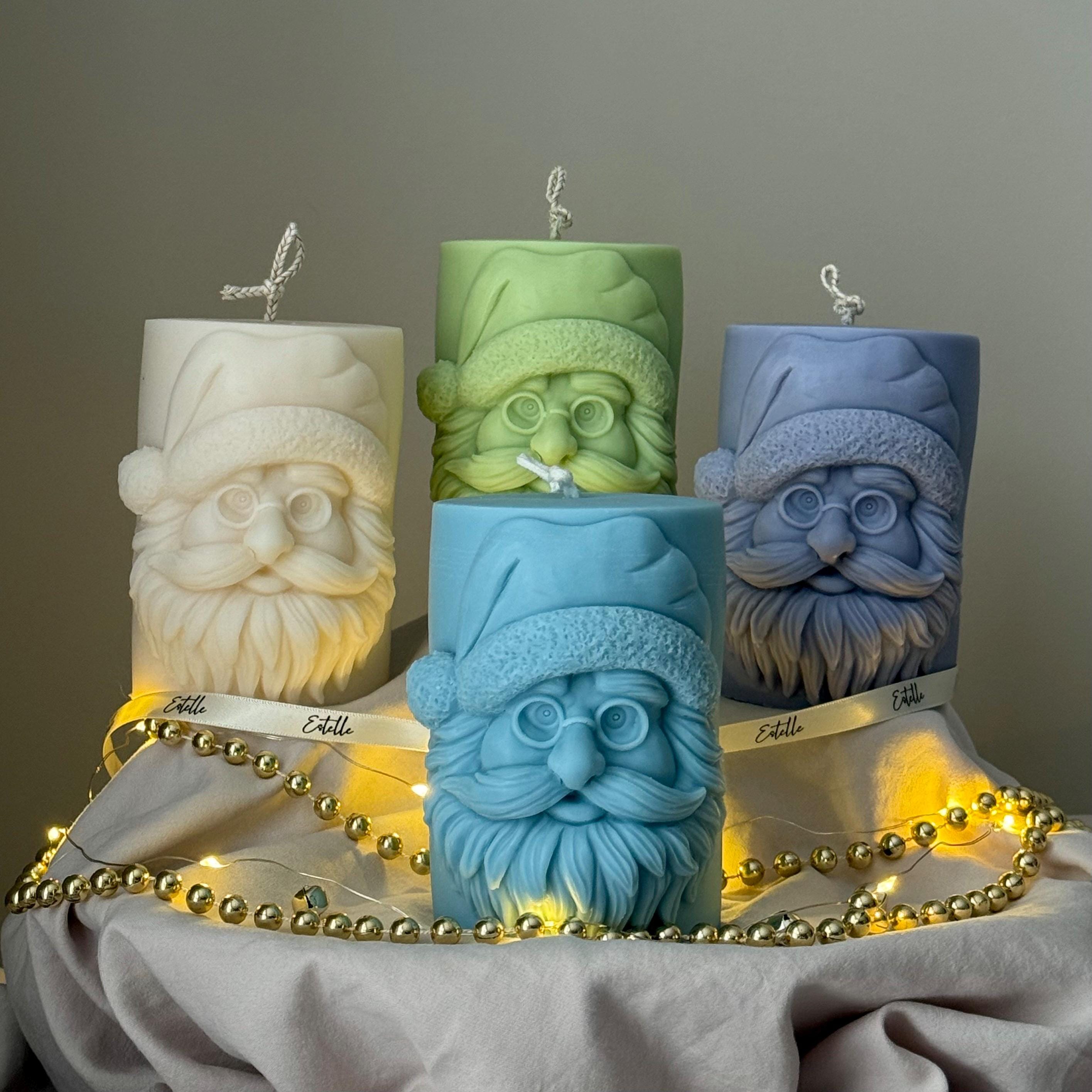 Four candles with Santa Claus faces on a gray surface with string lights from Estelle Studios