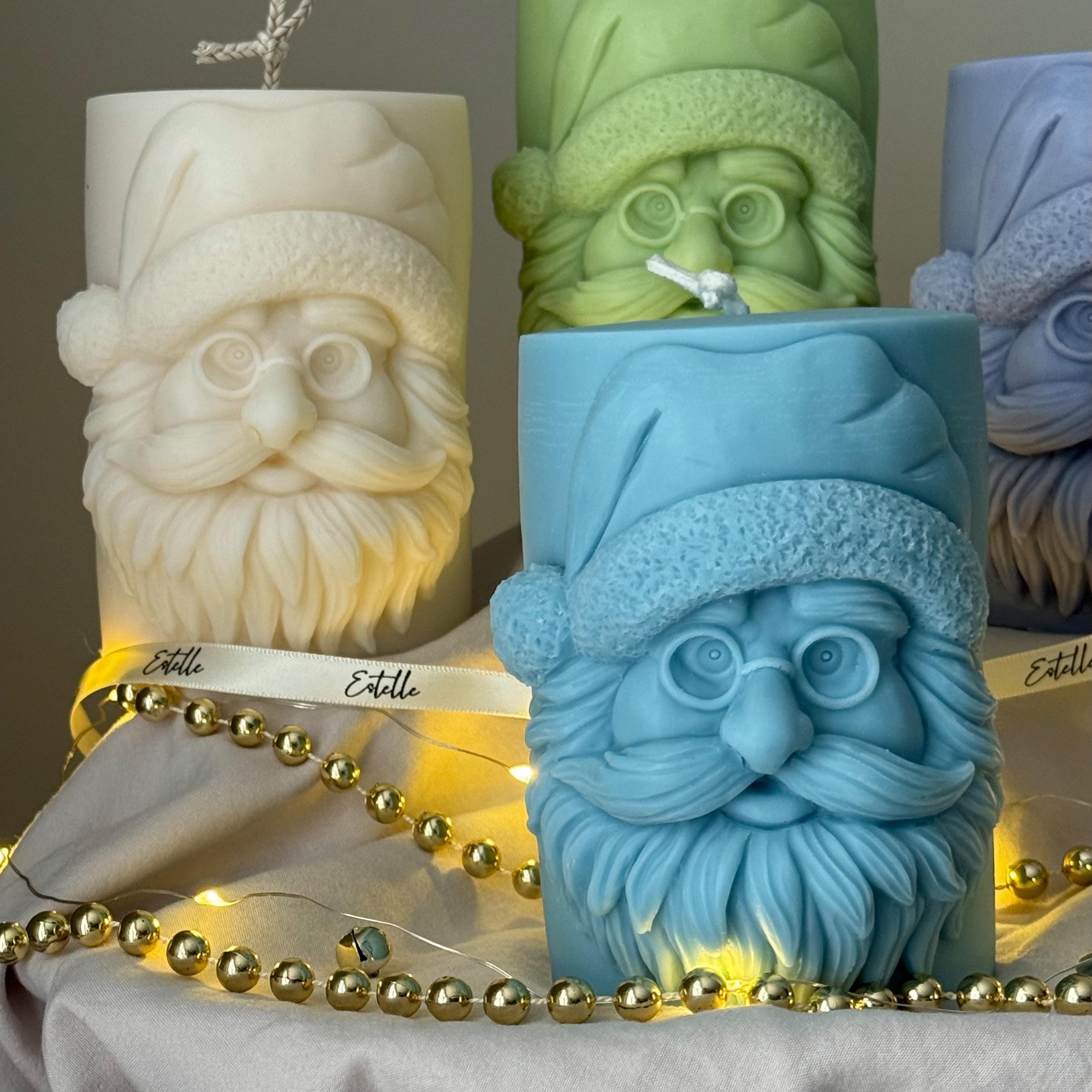 Four candles with Santa Claus faces on a gray surface with string lights from Estelle Studios