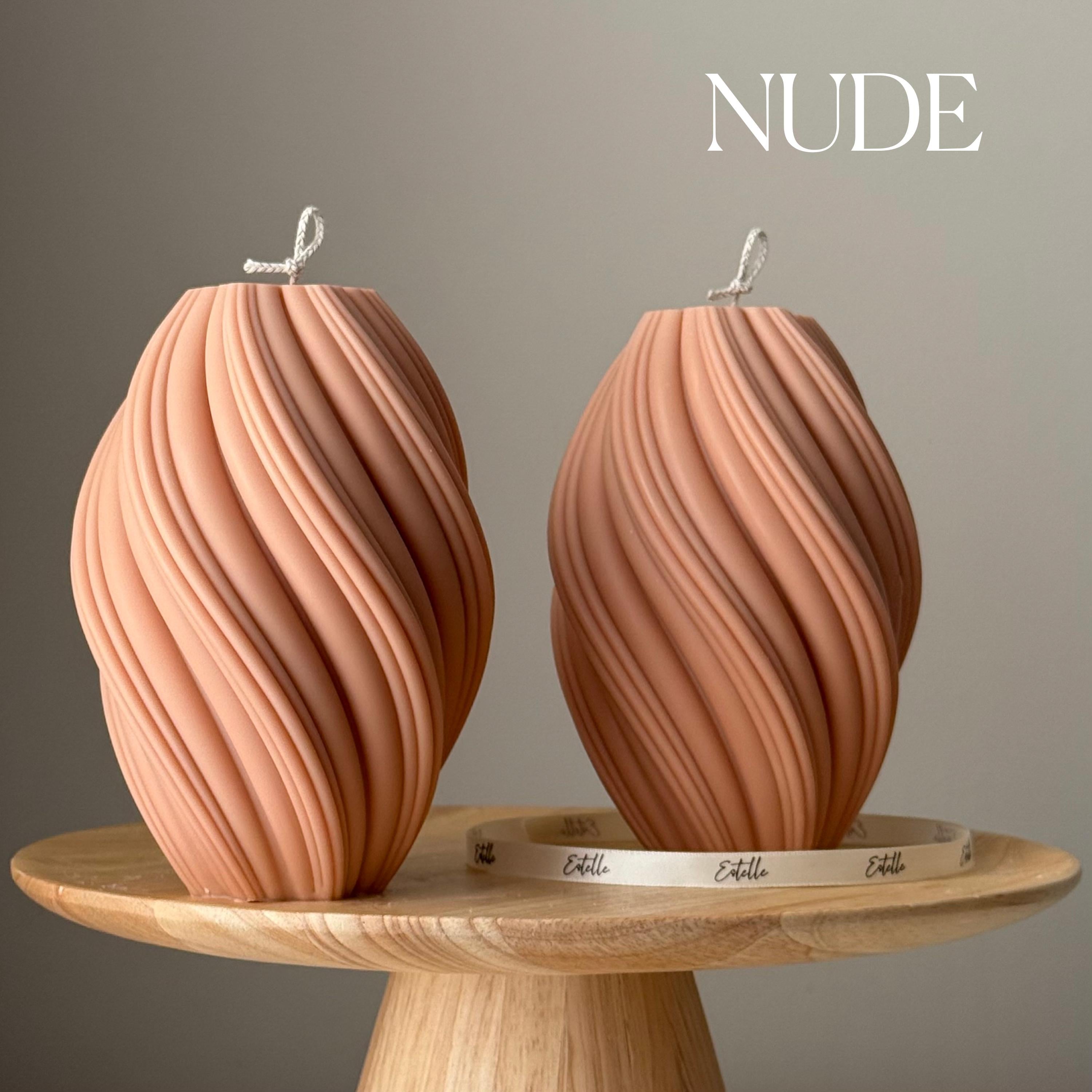 Two wavy-patterned candles on a wooden stand with 'NUDE' branding.