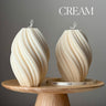 Two cream-colored candles with wavy texture on a wooden stand against a gray background.