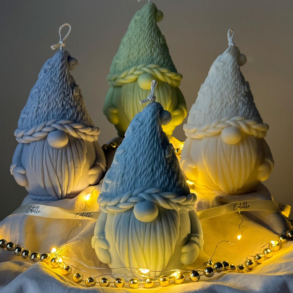 Four gnome-shaped candles with string lights on a dark background