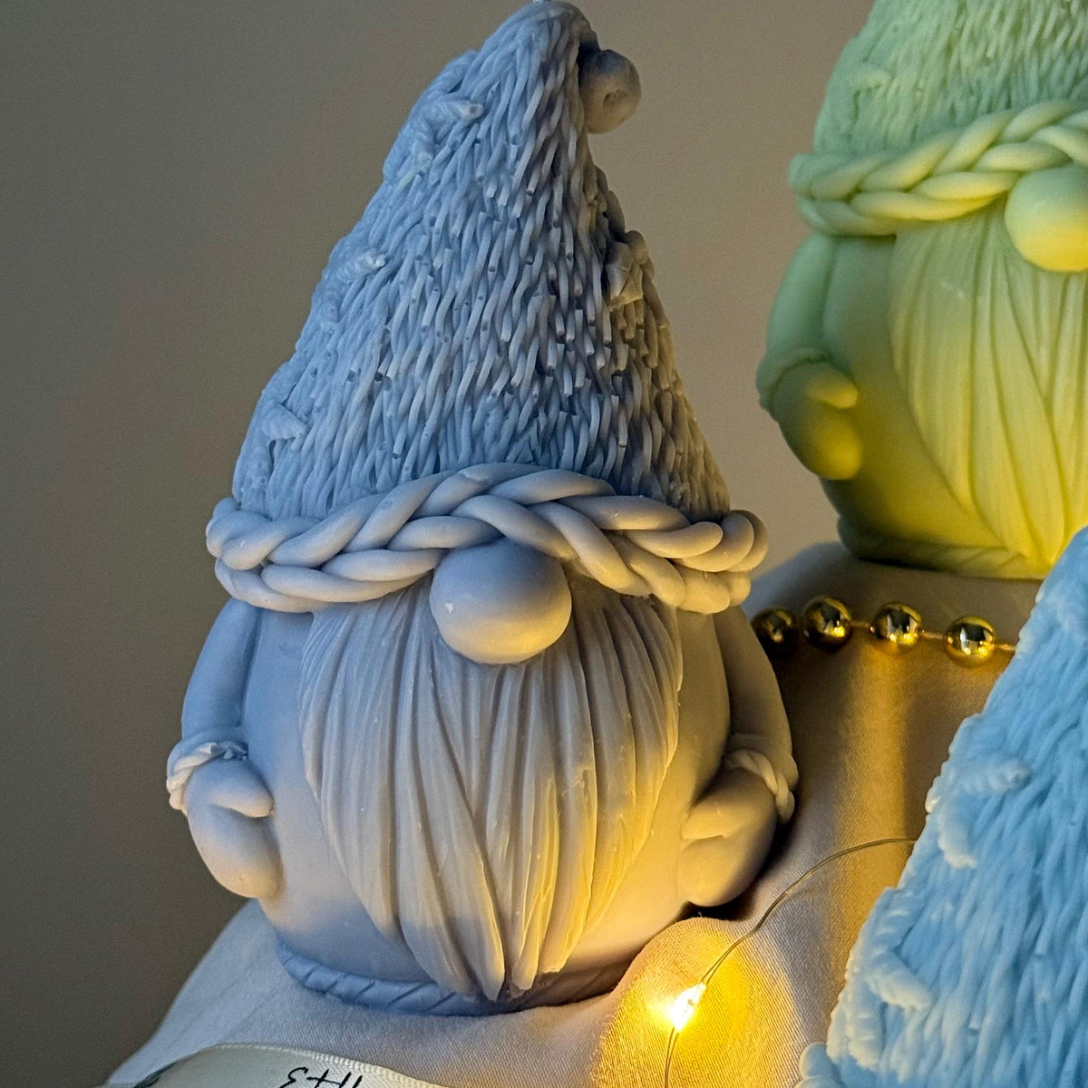 Two decorative gnomes with braided hair, one blue and one green, against a neutral background.