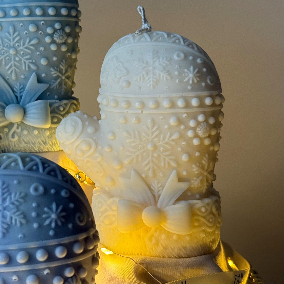 White Decorative candles with snowflake and bow designs, on a neutral background.