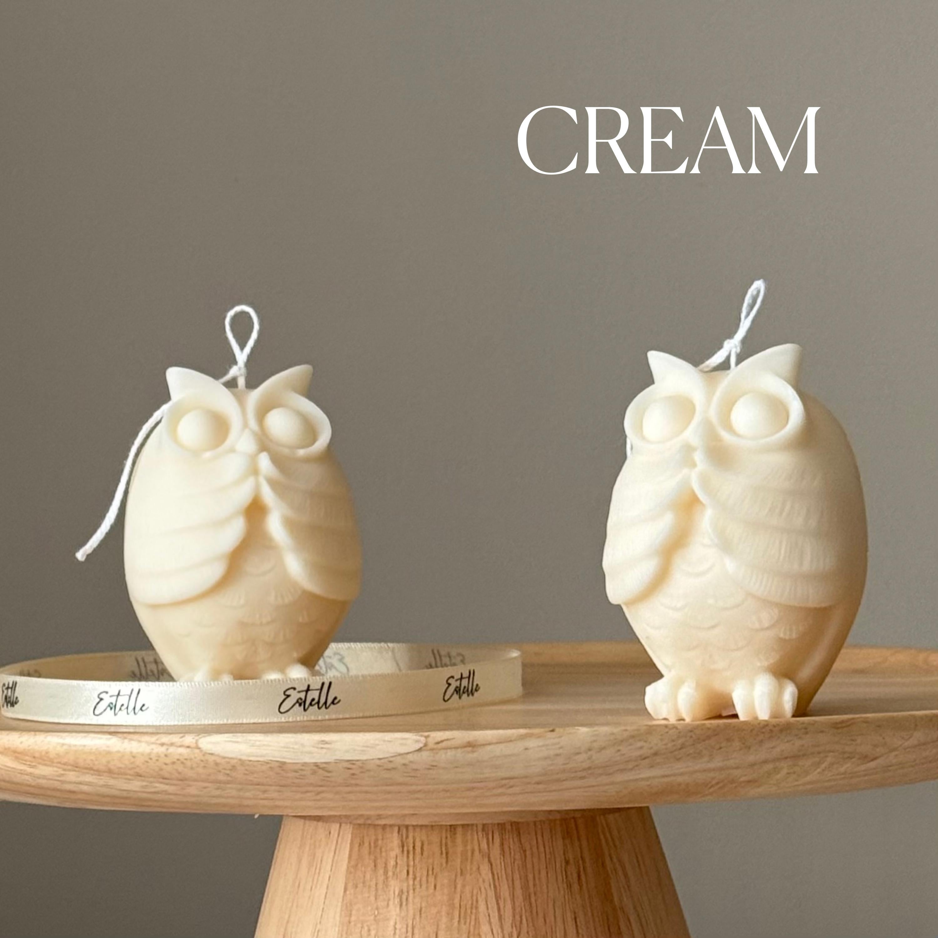 Two owl-shaped candles on a wooden surface with a neutral background