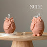 Two owl-shaped candles on a wooden stand with a neutral background